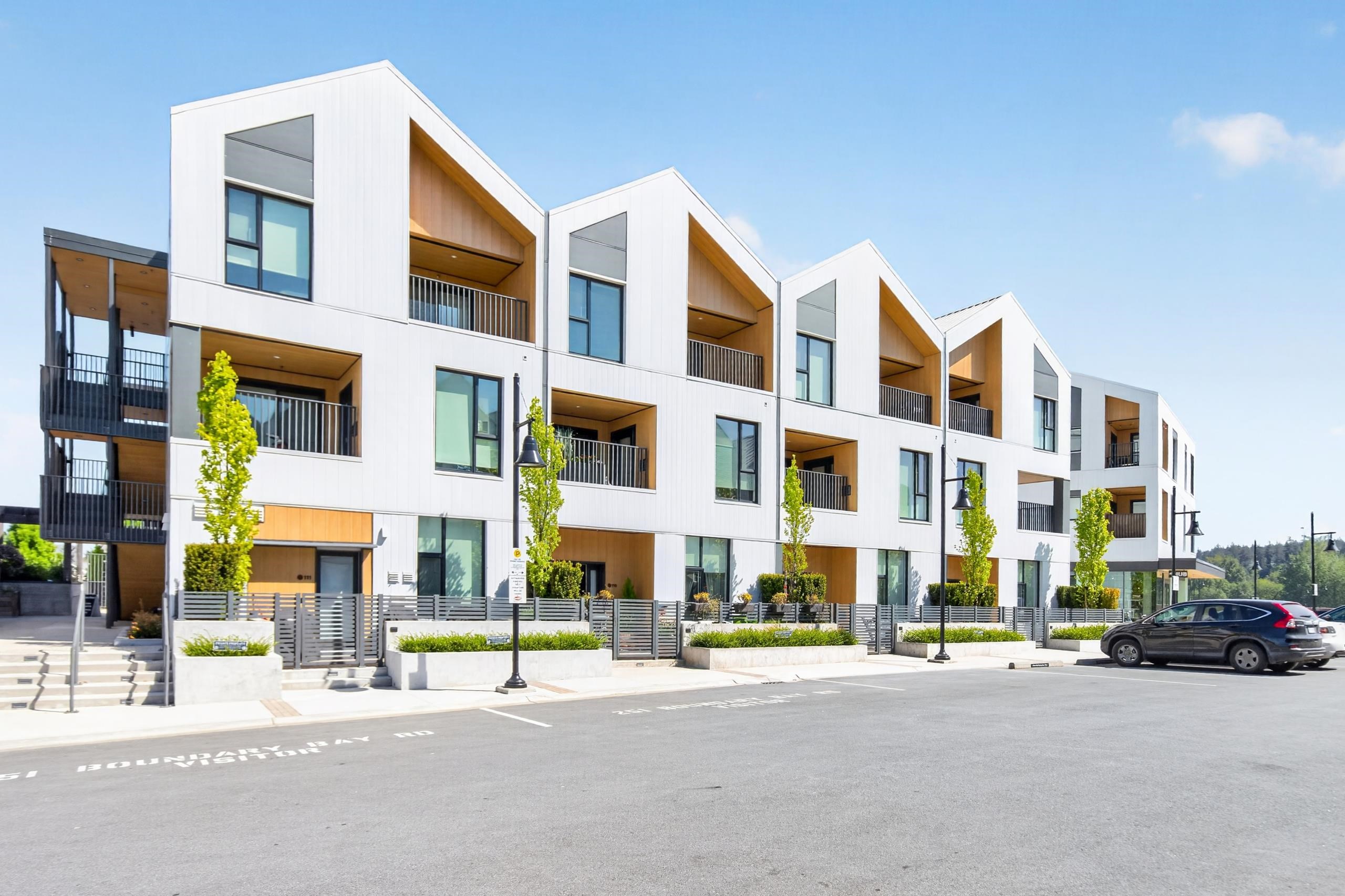Modern white apartment building with gabled façades, recessed balconies, and landscaped street frontage.