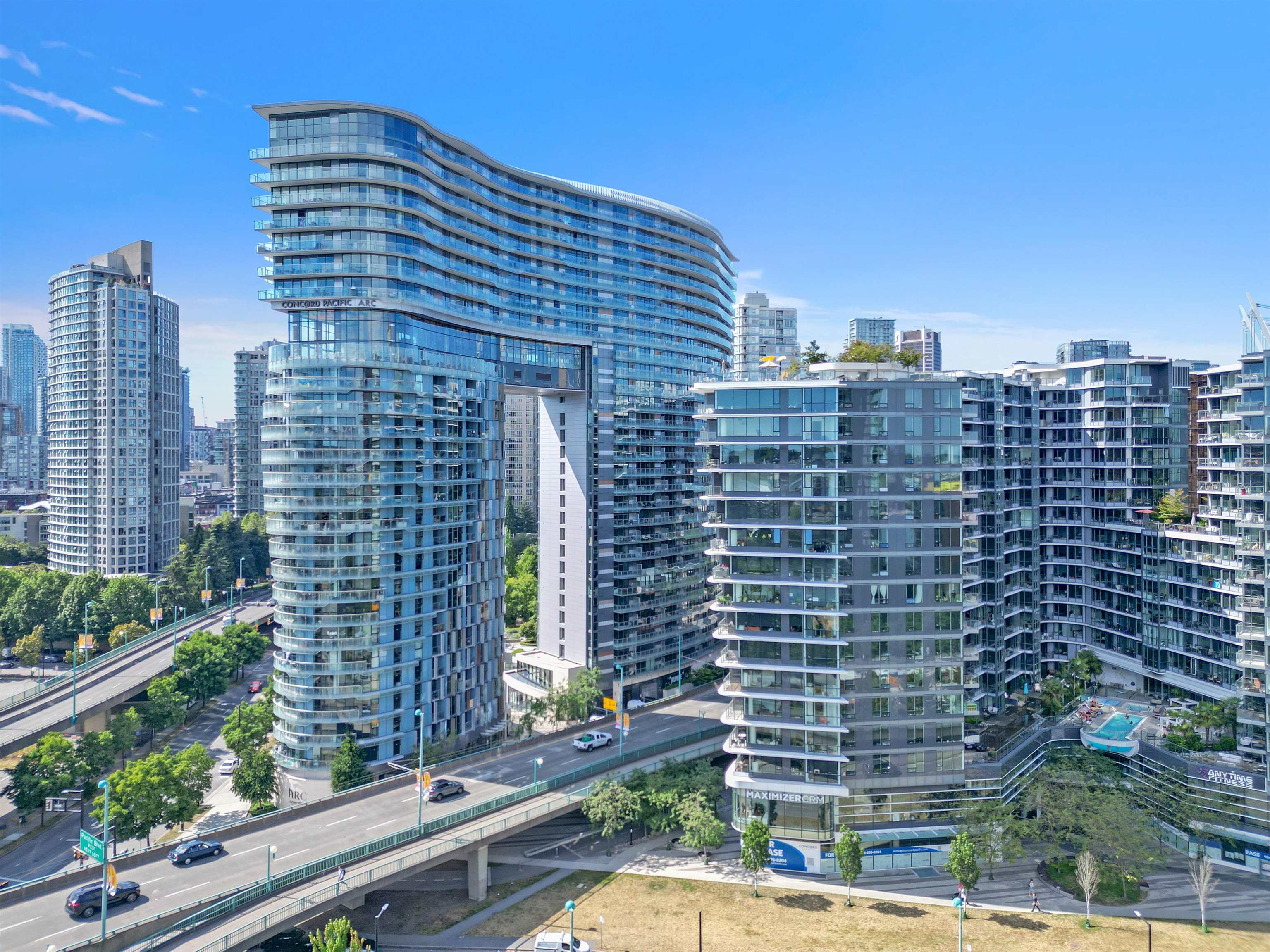 Curved glass Concord Pacific ARC tower among downtown high-rises, with an elevated roadway and courtyard pool.