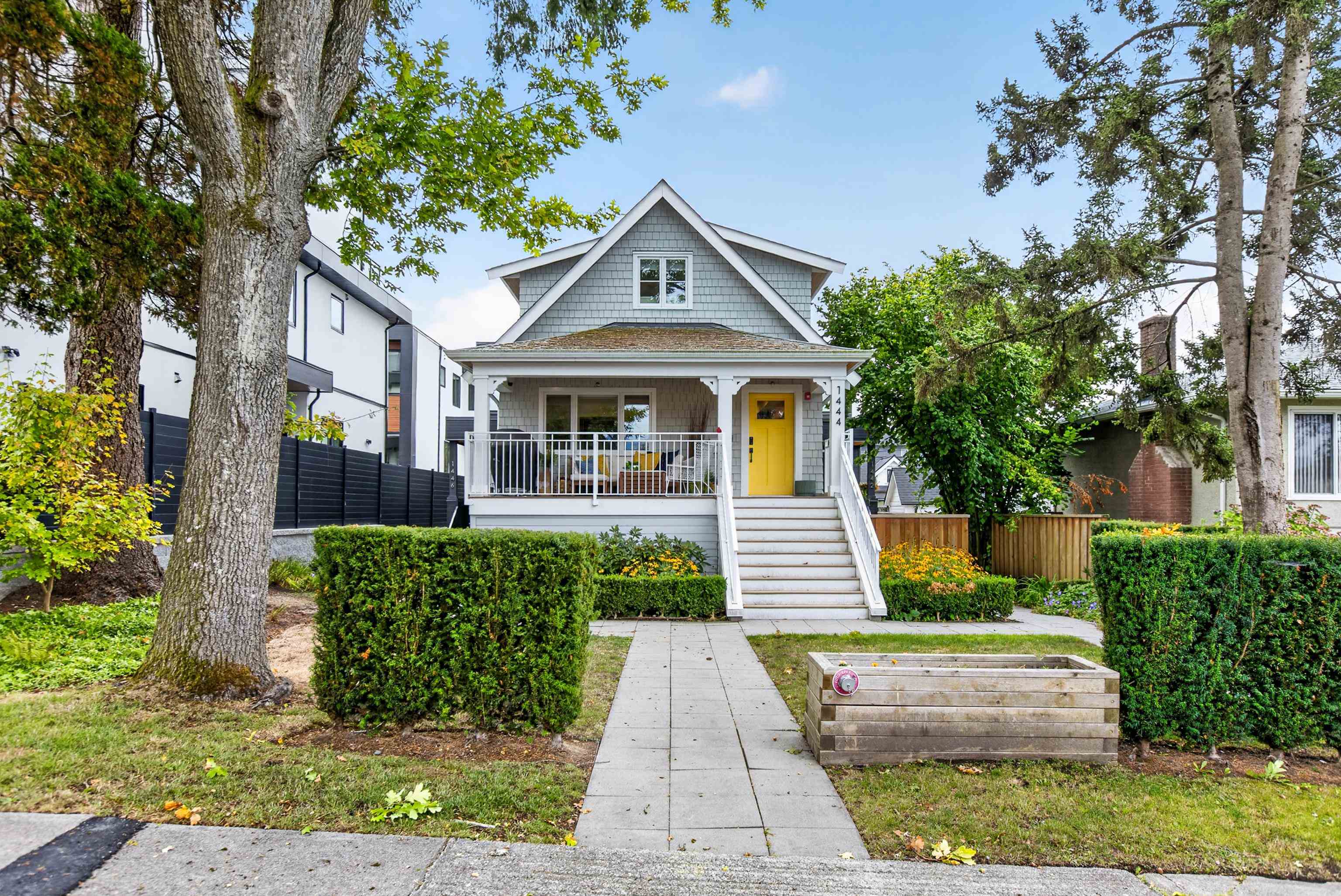 Gray gabled house with a covered porch, bright yellow door, and landscaped front yard.