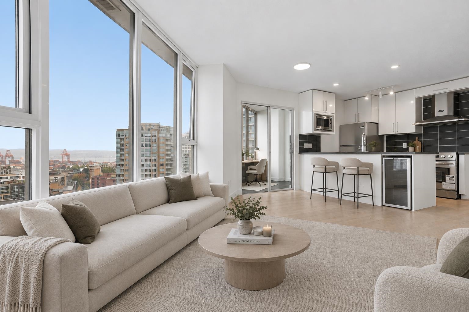 Furnished condo living room and kitchen with floor-to-ceiling windows overlooking city buildings and harbor cranes.