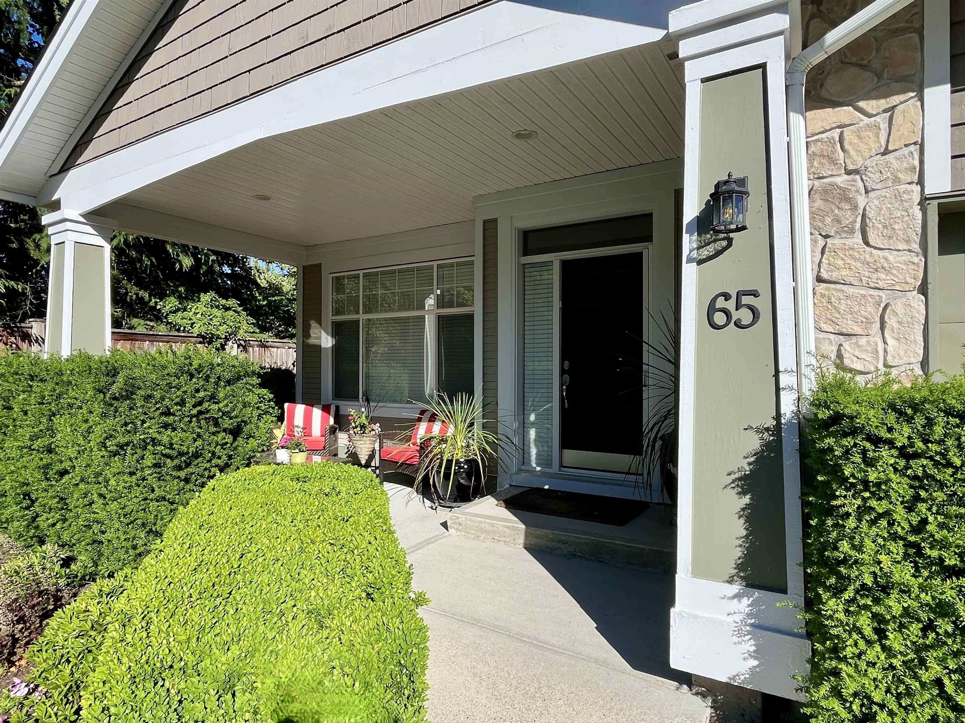 Home entrance with a covered porch, stone accents, red-striped chairs, and the number 65.