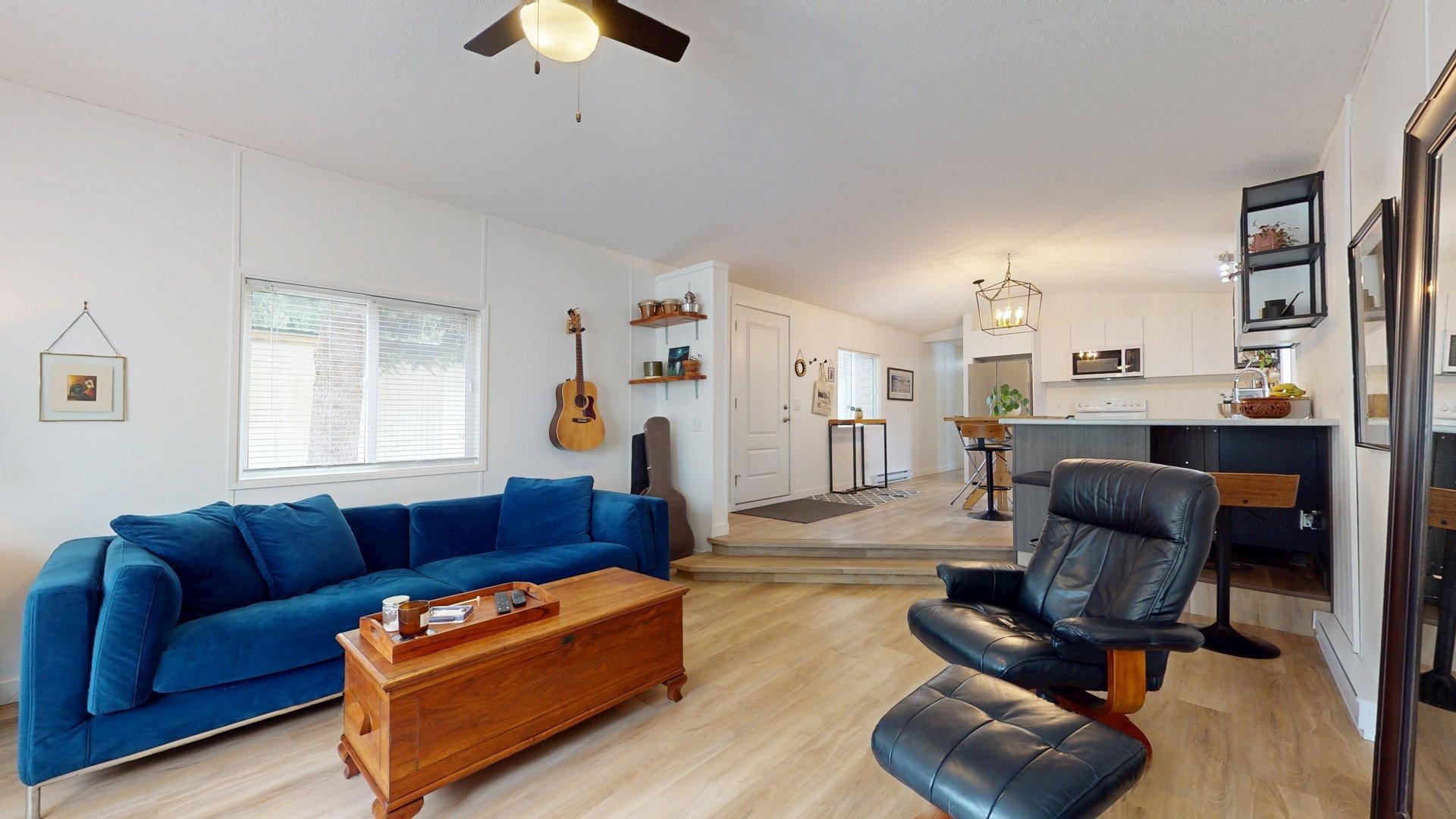 Open-plan living room and kitchen with a blue sofa, black leather lounge chair, and light wood floors.