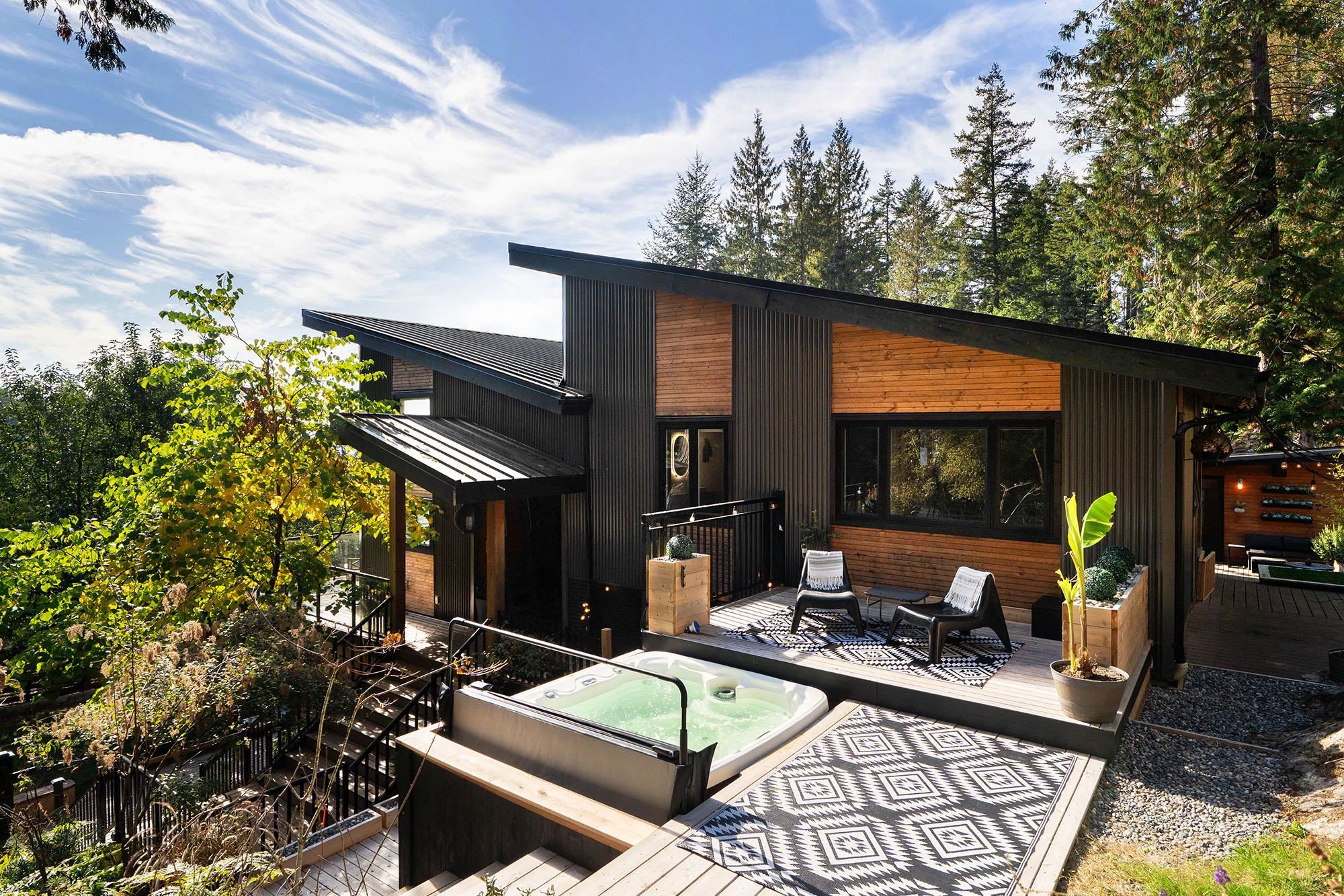 Modern wood-and-metal home with a furnished deck and hot tub among trees