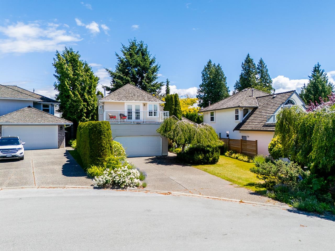 White raised home with an elevated deck, garage, and landscaped front yard.