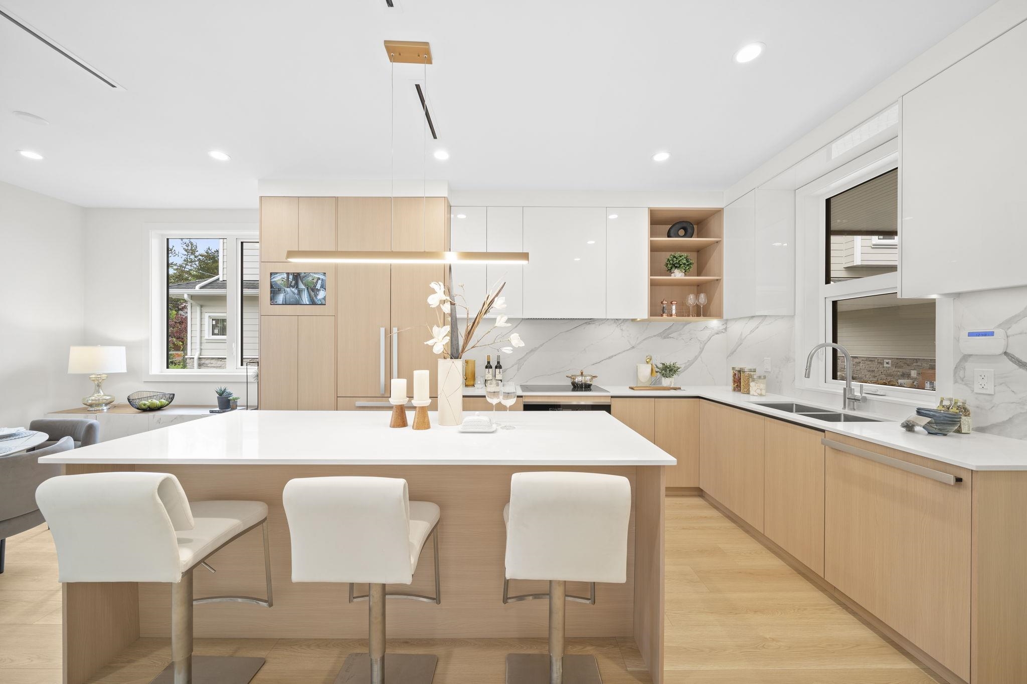 Modern kitchen with pale wood cabinets, a large white island, and three upholstered stools.