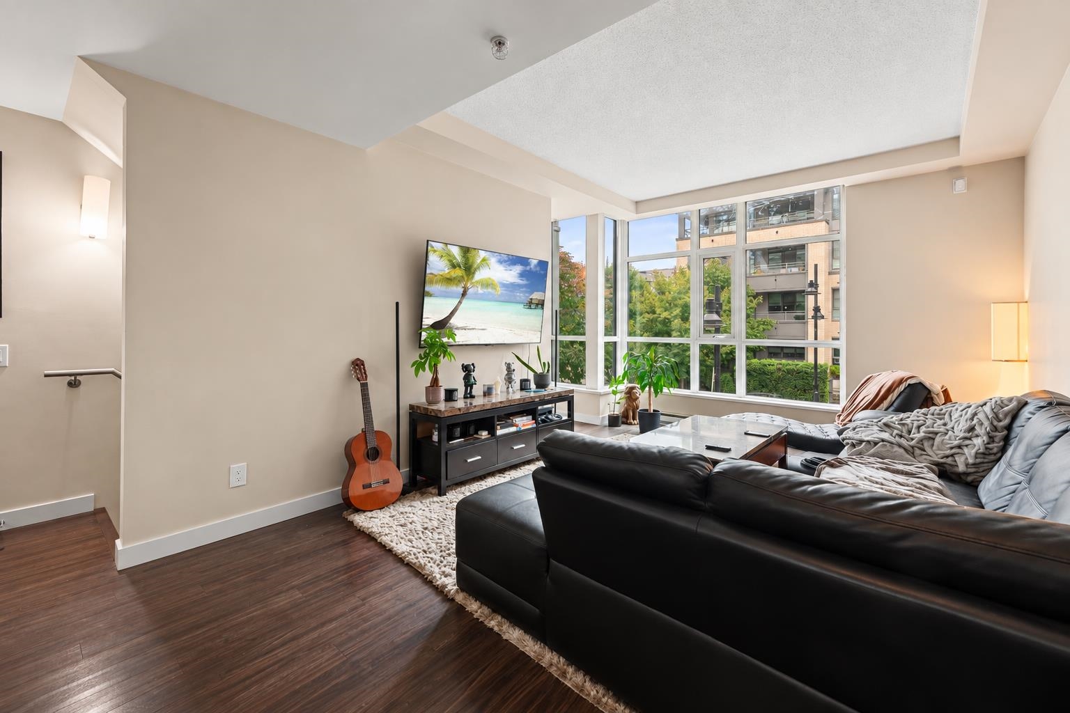 Living room with a black leather sectional, large windows, and a guitar beside the media console.