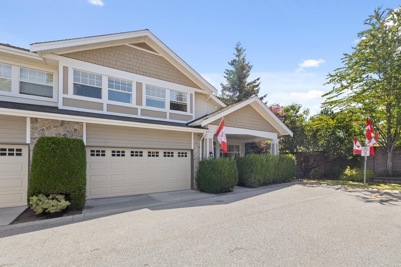 Two-story beige home with a double garage, stone accents, trimmed hedges, and Canadian flags.