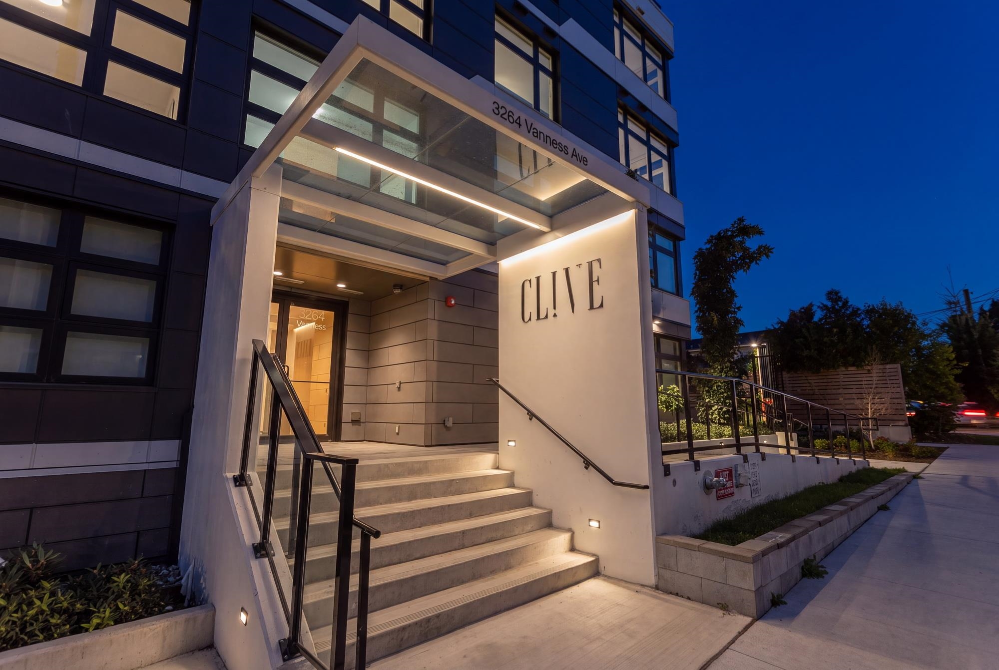 Modern apartment entrance with illuminated steps, glass canopy, and CL!VE sign at dusk.