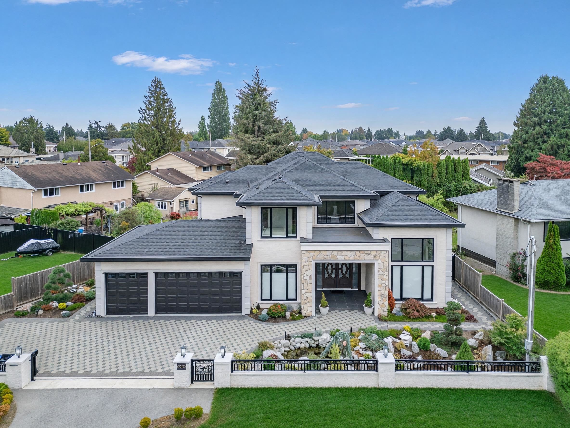 Aerial view of a modern two-story home with stone entry accents, a double garage, and a landscaped gated yard.