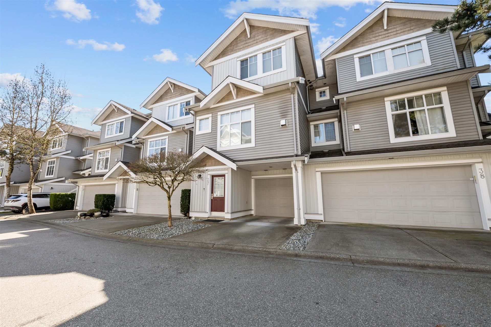 Row of gray townhouses with attached garages, peaked roofs, and small leafless trees.