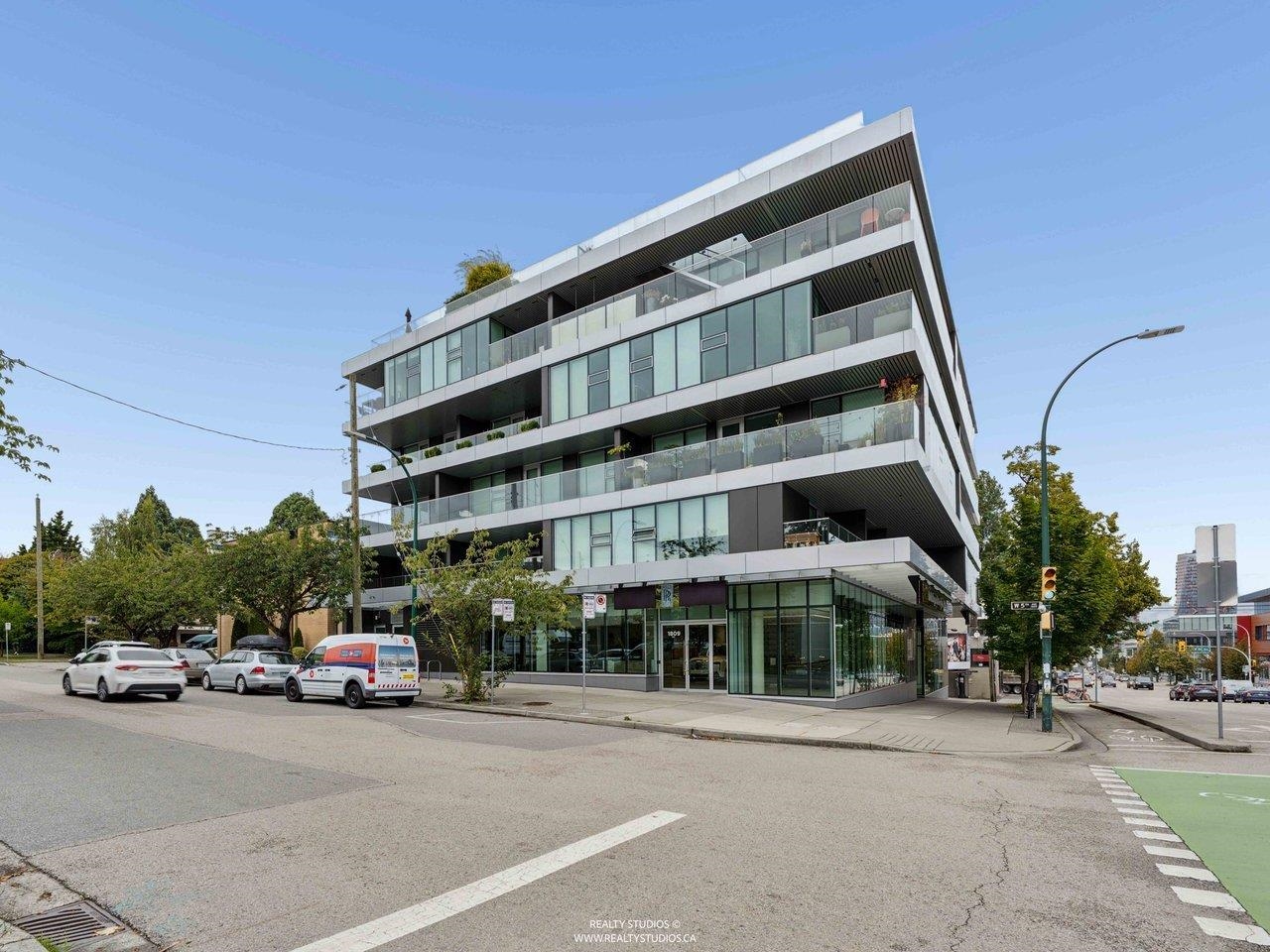 Modern Vancouver corner building with glass balconies and ground-floor storefronts.