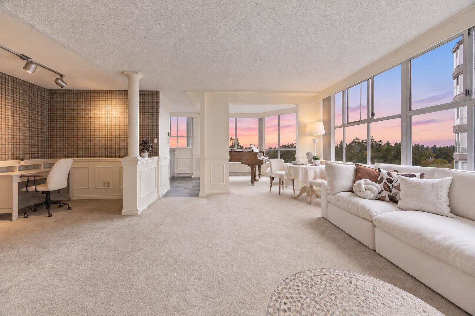 Furnished condo living room with floor-to-ceiling windows overlooking treetops at sunset.