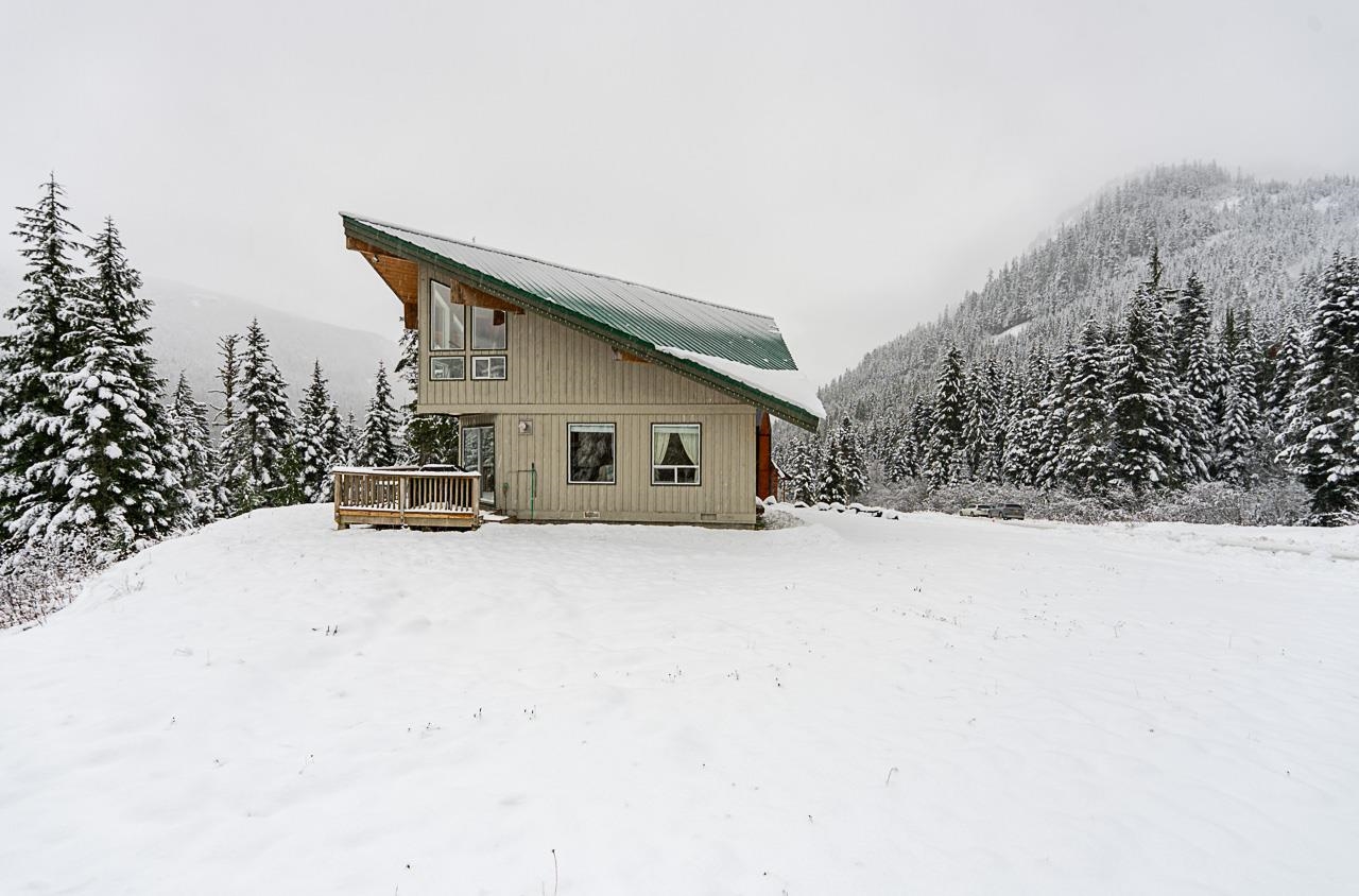 Modern cabin with a steep green roof and wooden deck in a snowy clearing among evergreen trees.