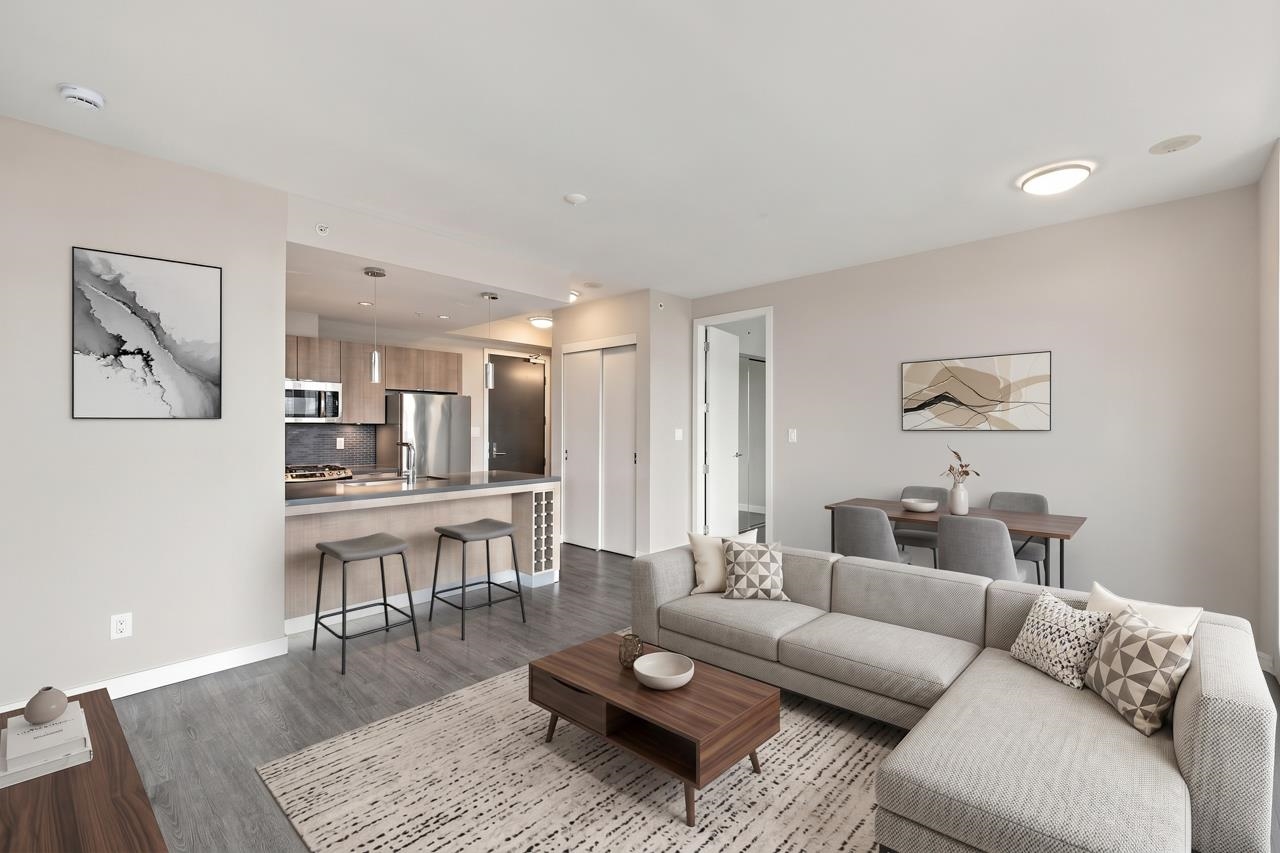 Open-plan condo living room with a gray sectional, dining area, and kitchen with stainless steel appliances.