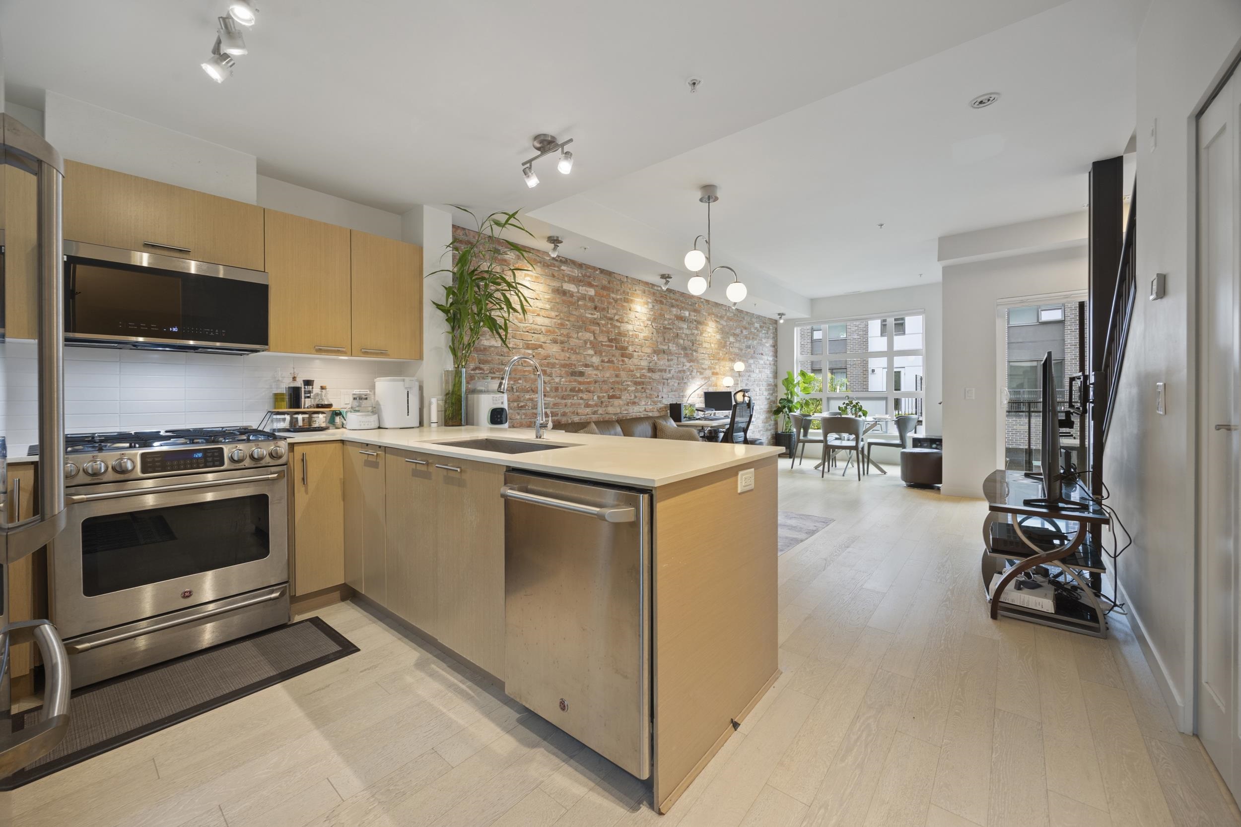 Open-plan kitchen with a large island, stainless steel appliances, and an exposed brick accent wall.