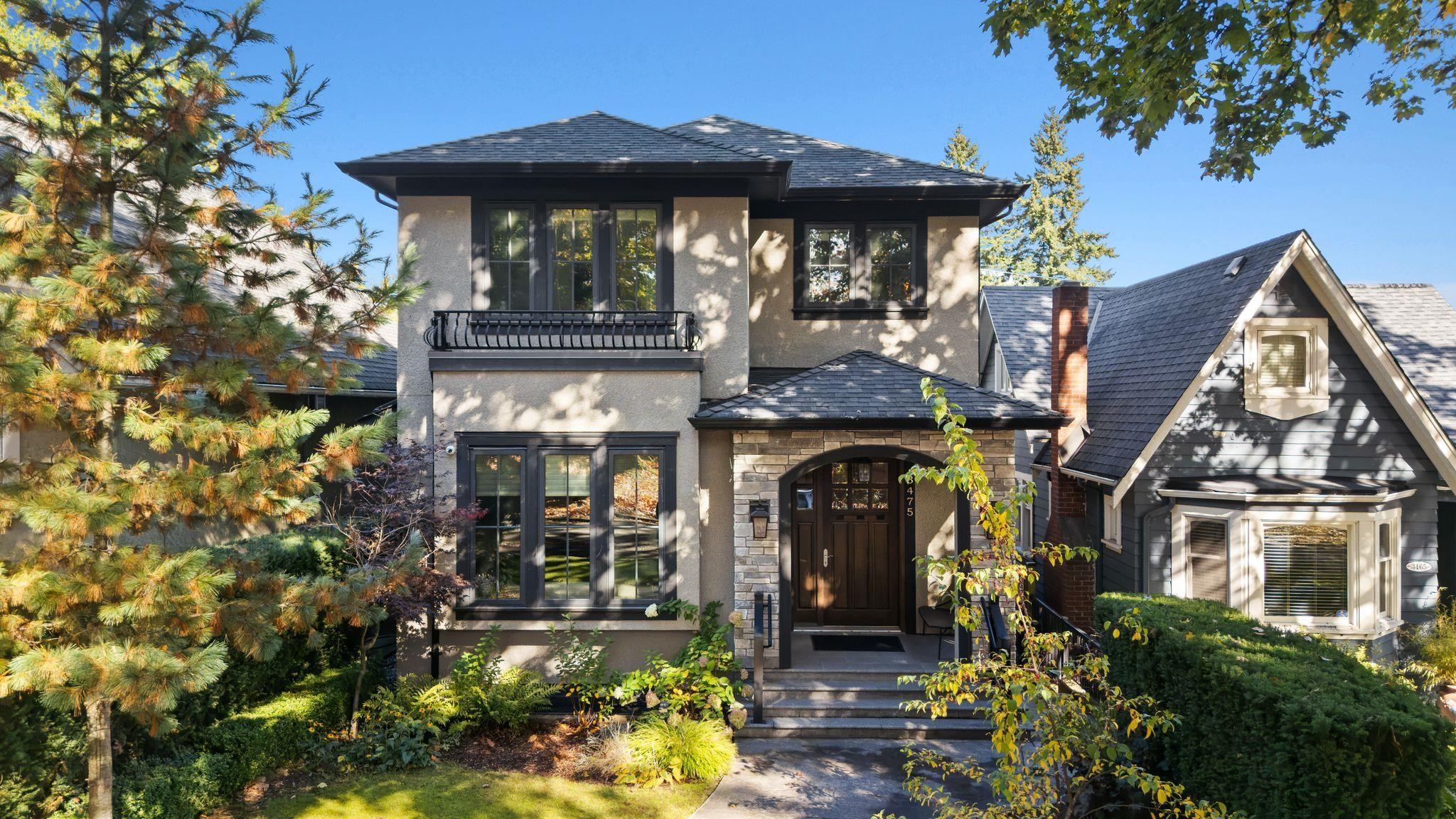 Two-storey gray home with a stone arched entry, small balcony, and mature landscaped garden.