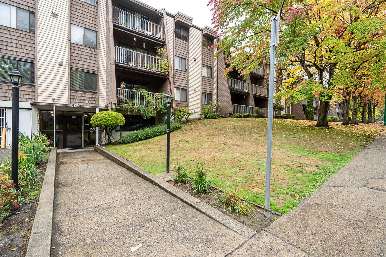 Condominium building with balconies, landscaped grounds, and an entrance walkway.