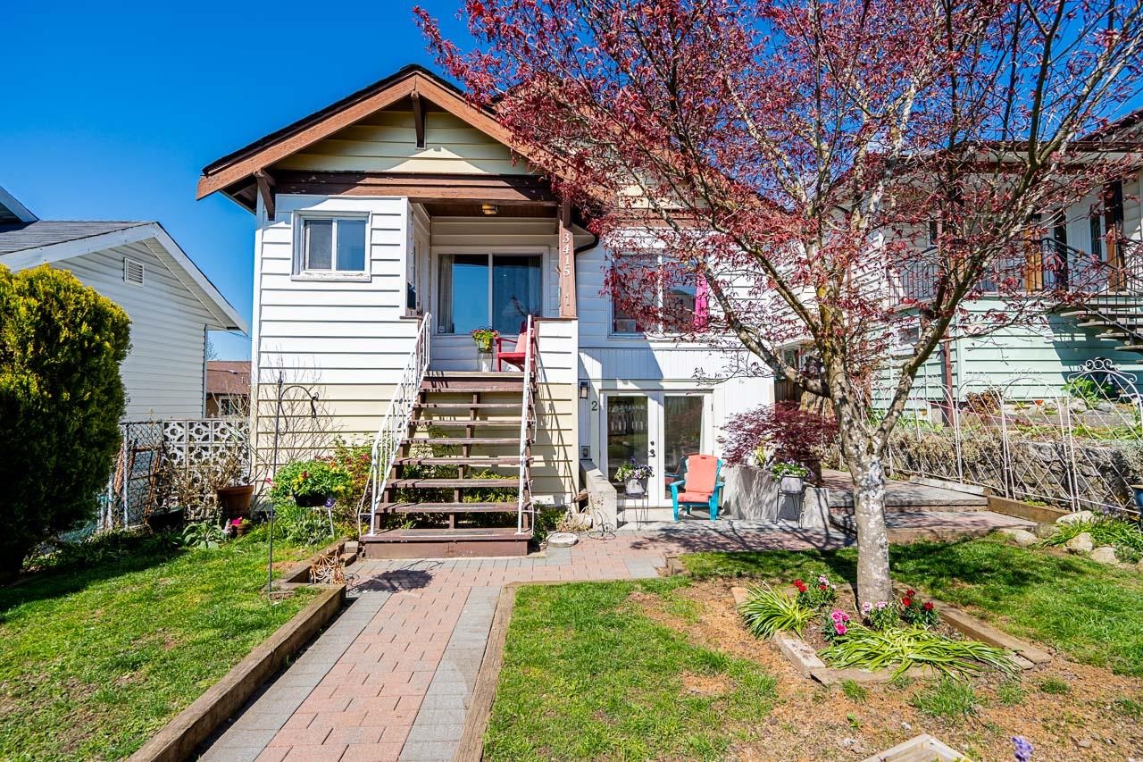 White house with a raised porch and brick walkway beneath a flowering tree.