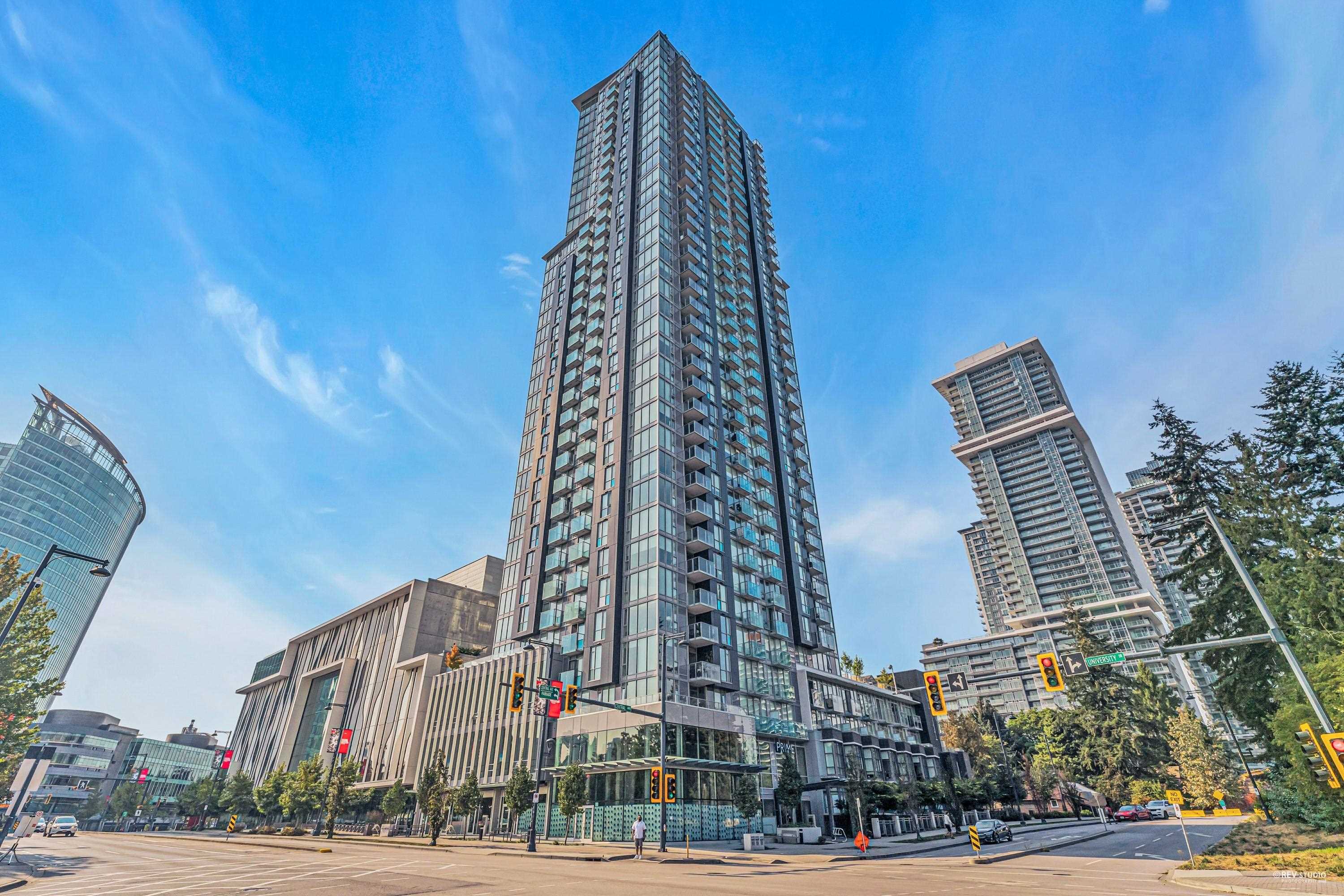 Modern high-rise condominium at a city intersection, framed by neighboring towers beneath a bright blue sky.