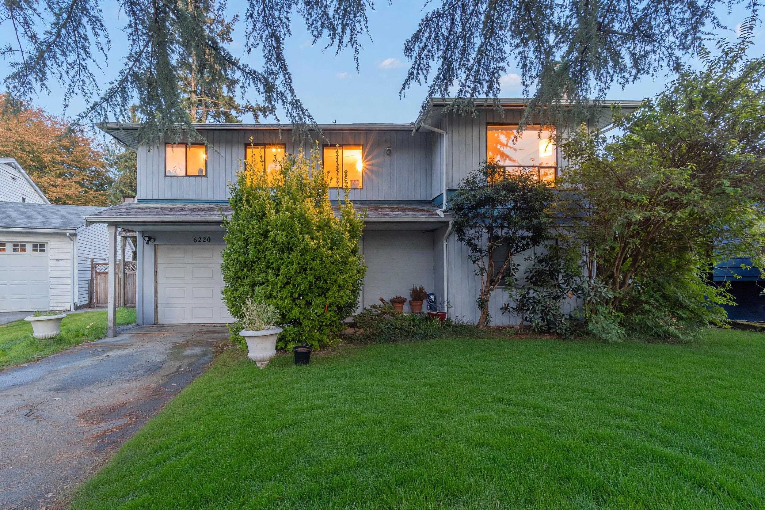 Two-story gray house with warmly lit windows, a garage, and a broad green lawn.