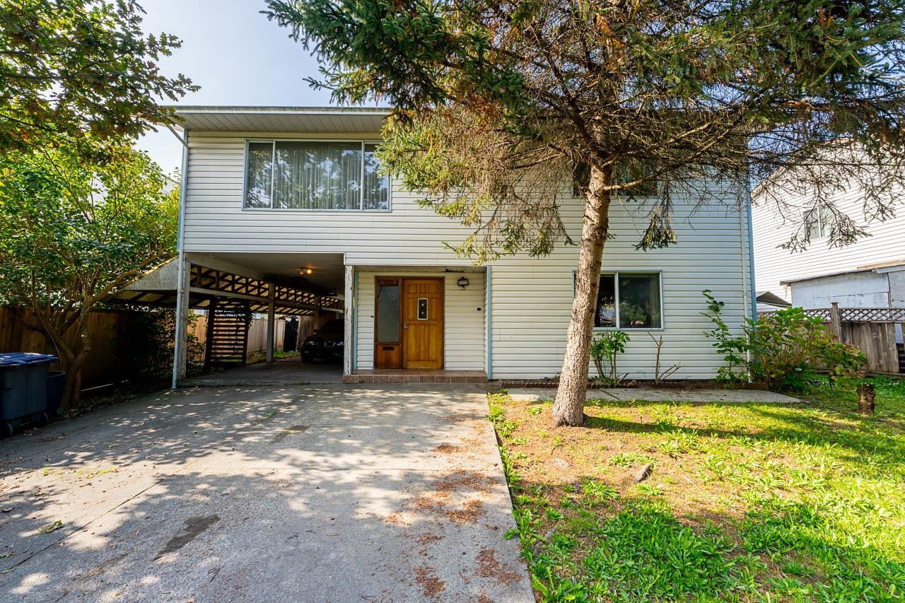 Two-story house with a covered carport, wooden front door, and mature trees.