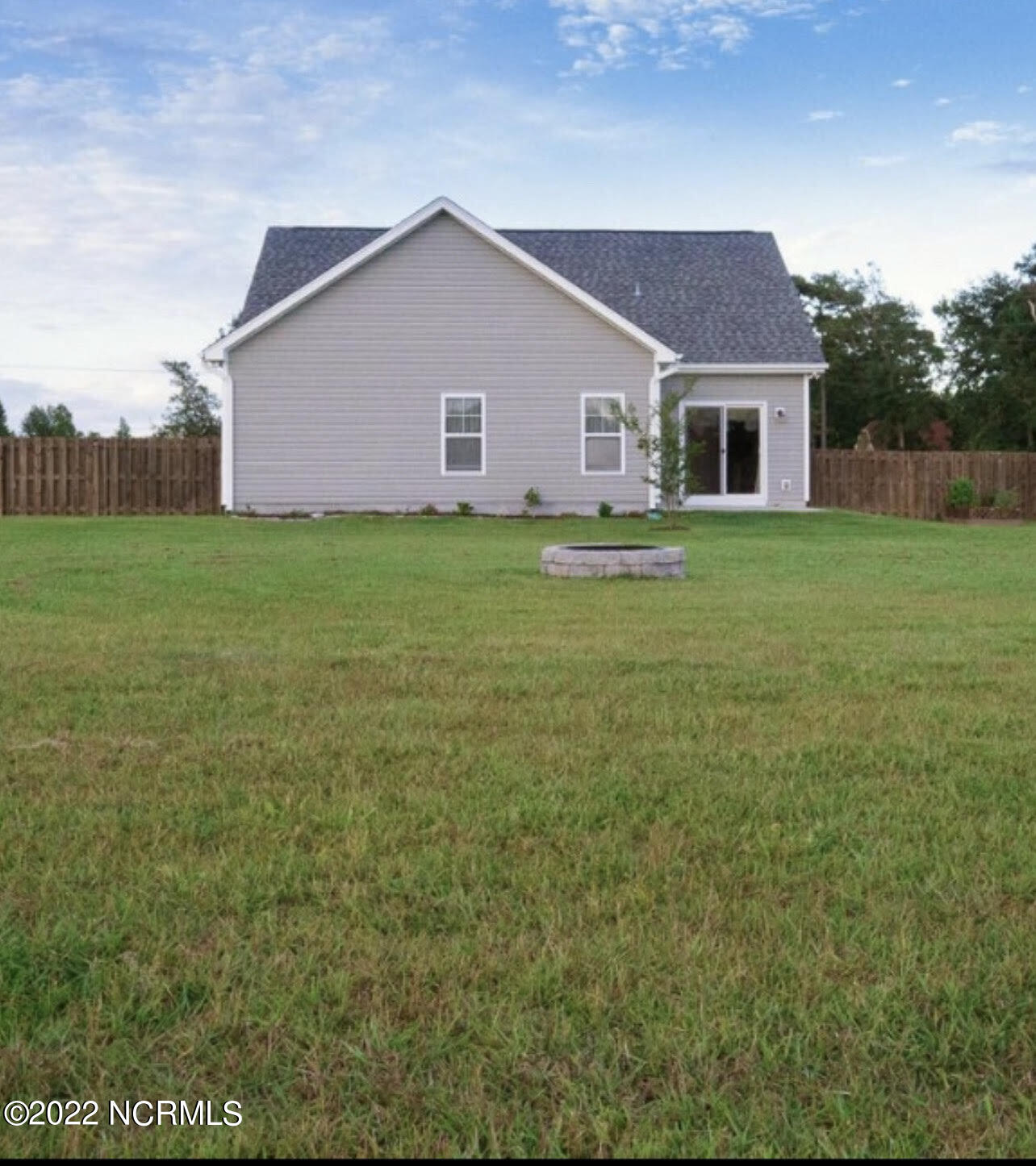Gray-sided house with a fenced backyard, broad lawn, and low circular stone feature.