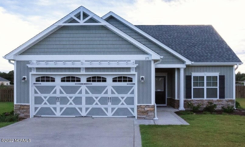 Blue-gray house with a white barn-style double garage door, front gables, stone accents, and lawn.
