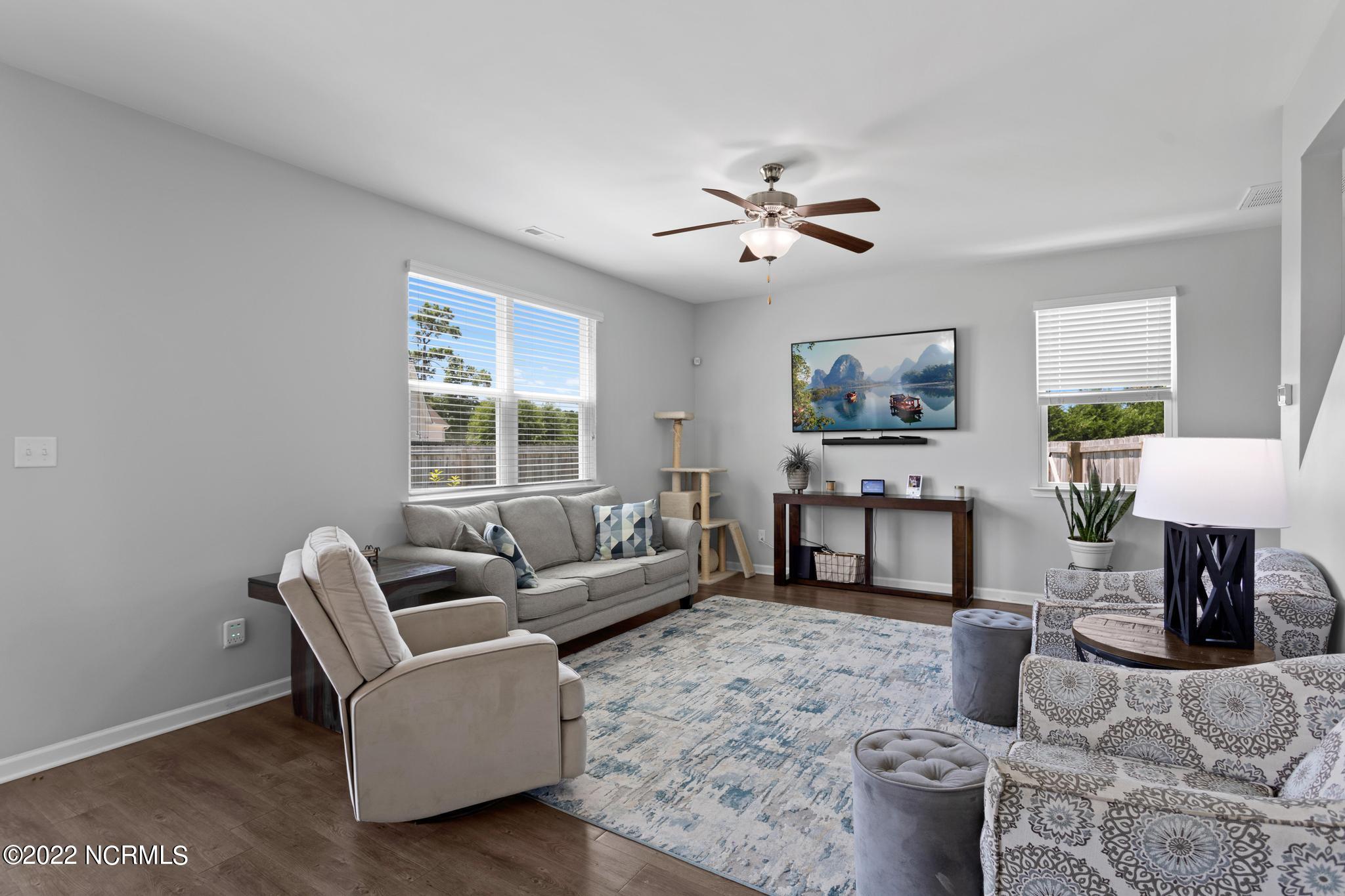 Furnished living room with gray sofa, patterned chairs, ceiling fan, and blue-gray area rug.
