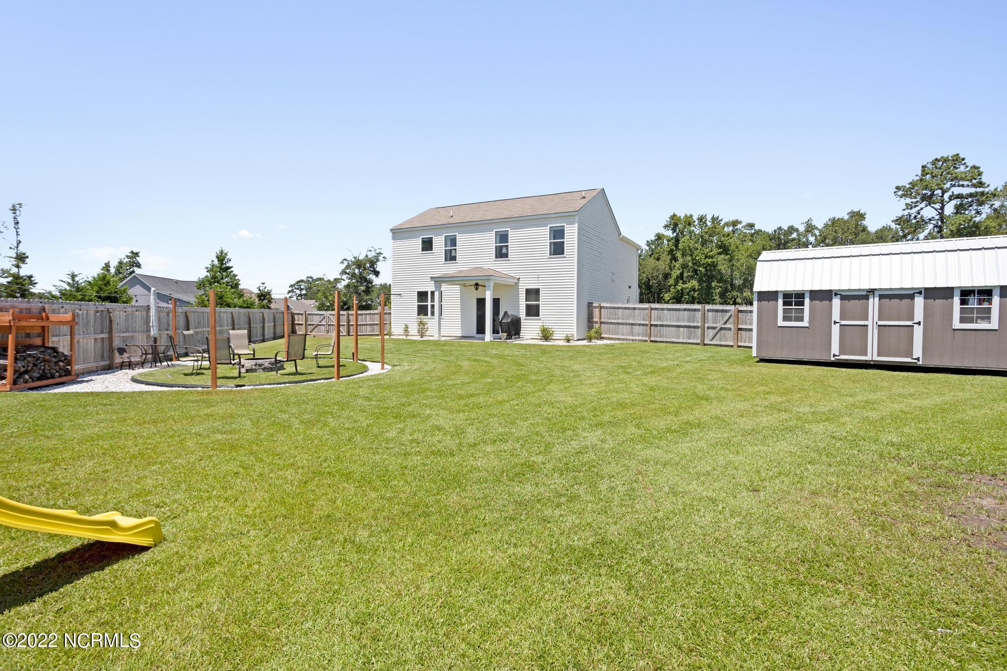 Fenced backyard with a broad lawn, detached shed, fire-pit seating area, and yellow slide.