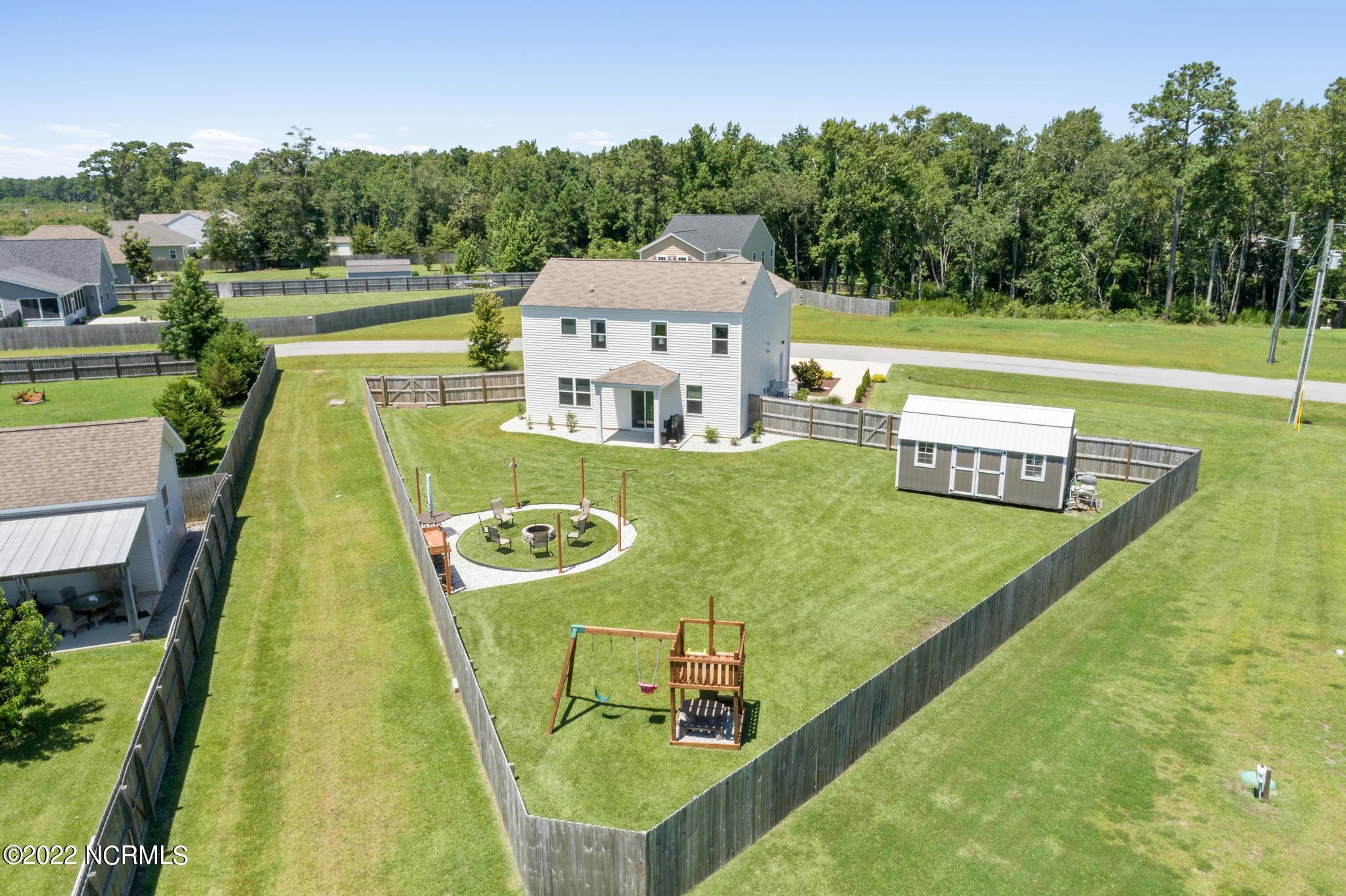Aerial view of a fenced backyard with a shed, playset, and circular fire pit seating area.