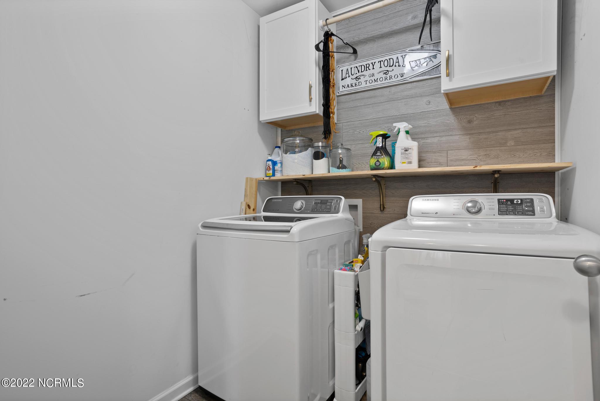 Laundry room with a white washer and dryer, wood-look backsplash, and storage shelf.