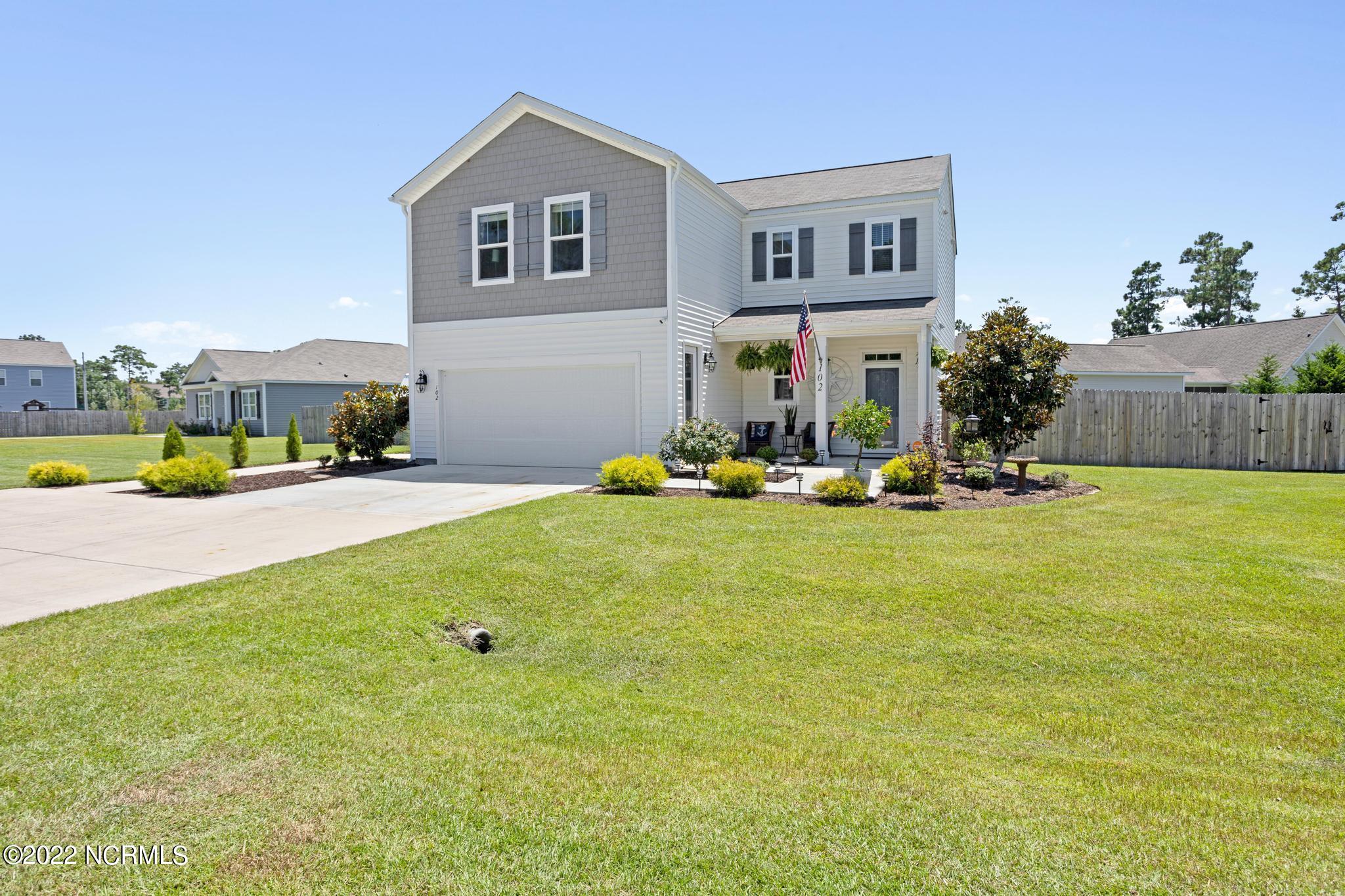Two-story gray and white home with an attached garage, landscaped lawn, and American flag by the front door.