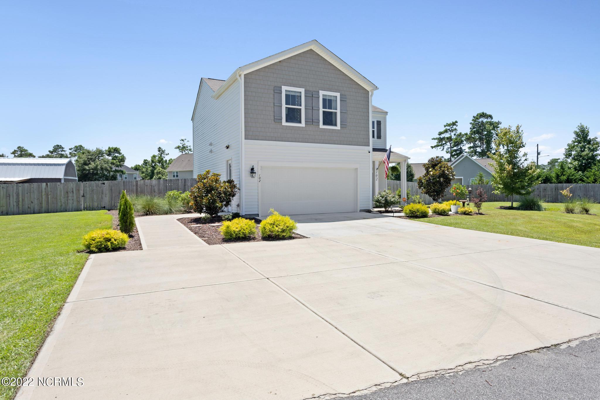 Two-story gray-and-white house with a double garage, wide driveway, landscaped yard, and American flag.