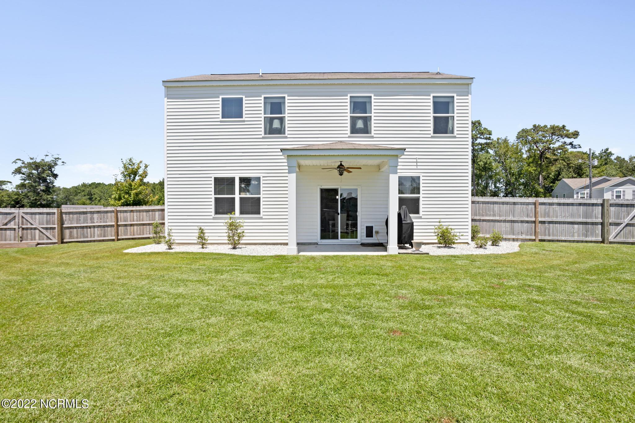 Two-story white house with a covered patio and fenced, spacious lawn.