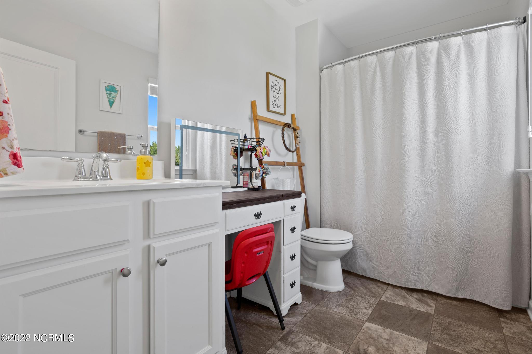 Bathroom with a white vanity, curtained shower, and small desk with a red chair.
