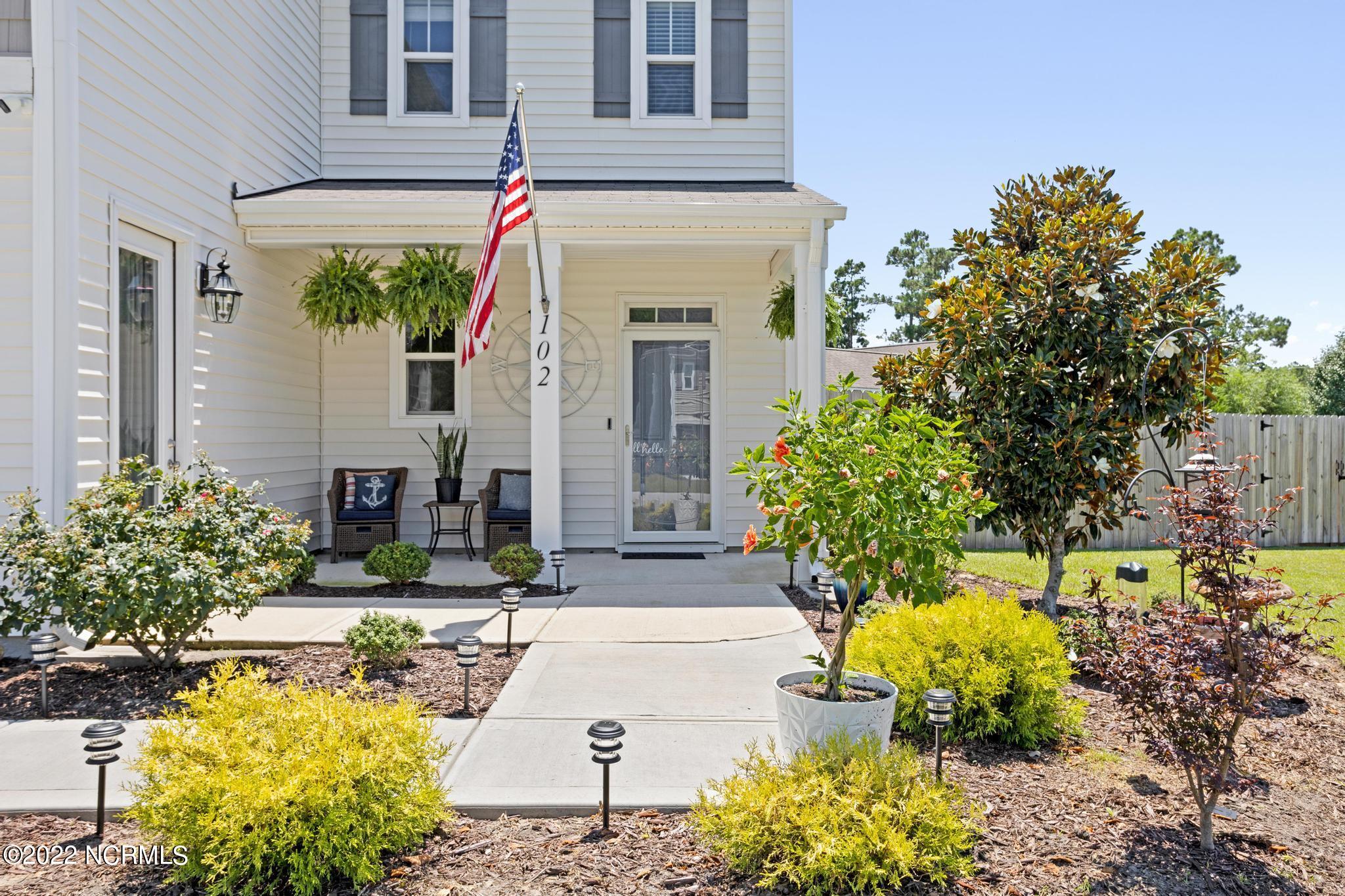 Two-story home with a covered porch, American flag, and landscaped front walkway.