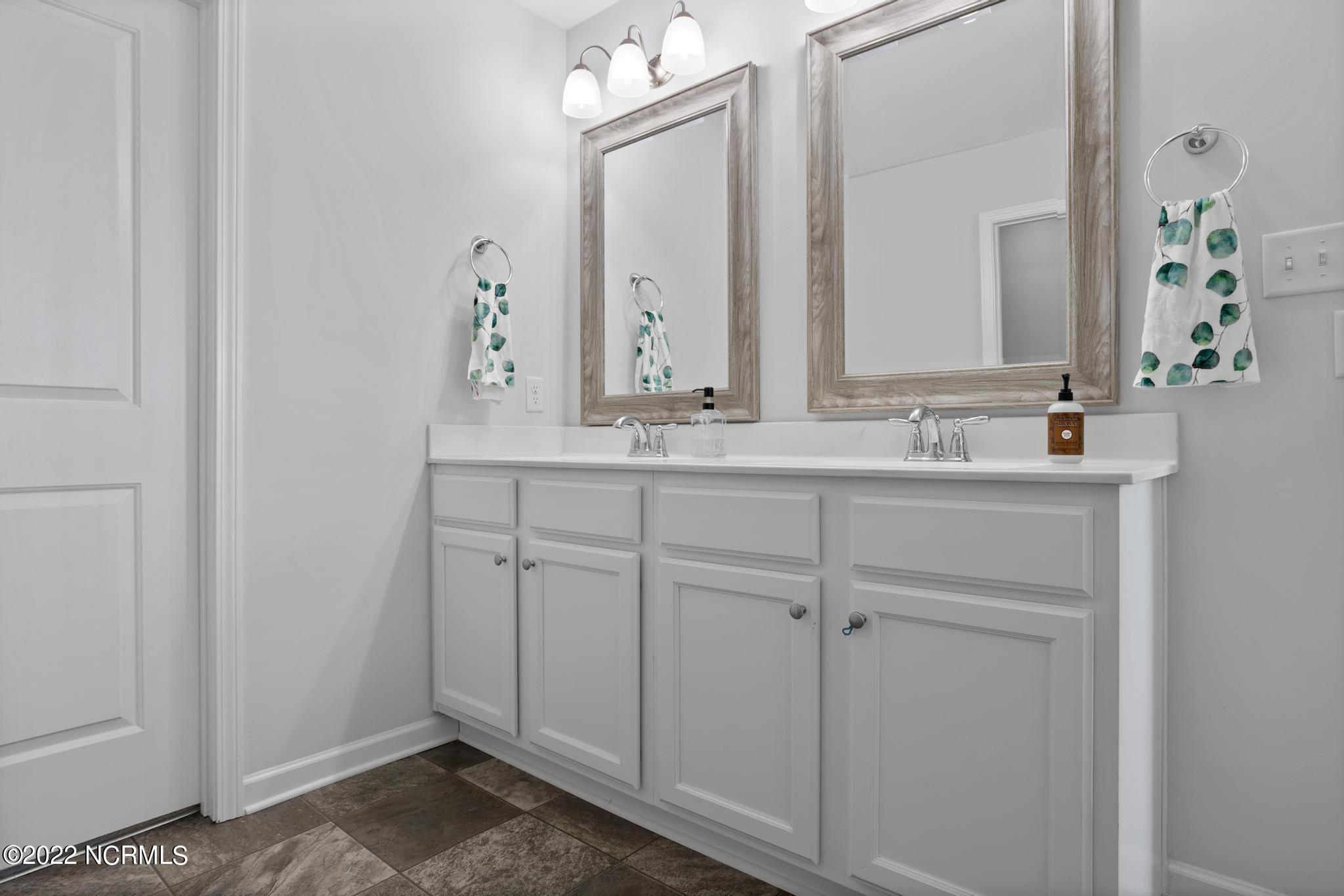 Bathroom with a white double vanity, two framed mirrors, and patterned hand towels.