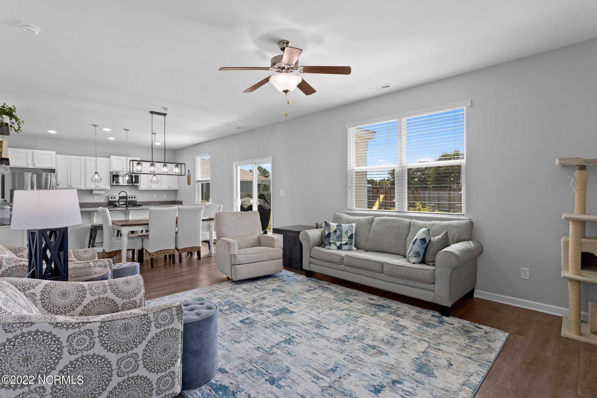 Open-plan living room and kitchen with gray seating, a blue-and-white rug, and a large window overlooking the yard.