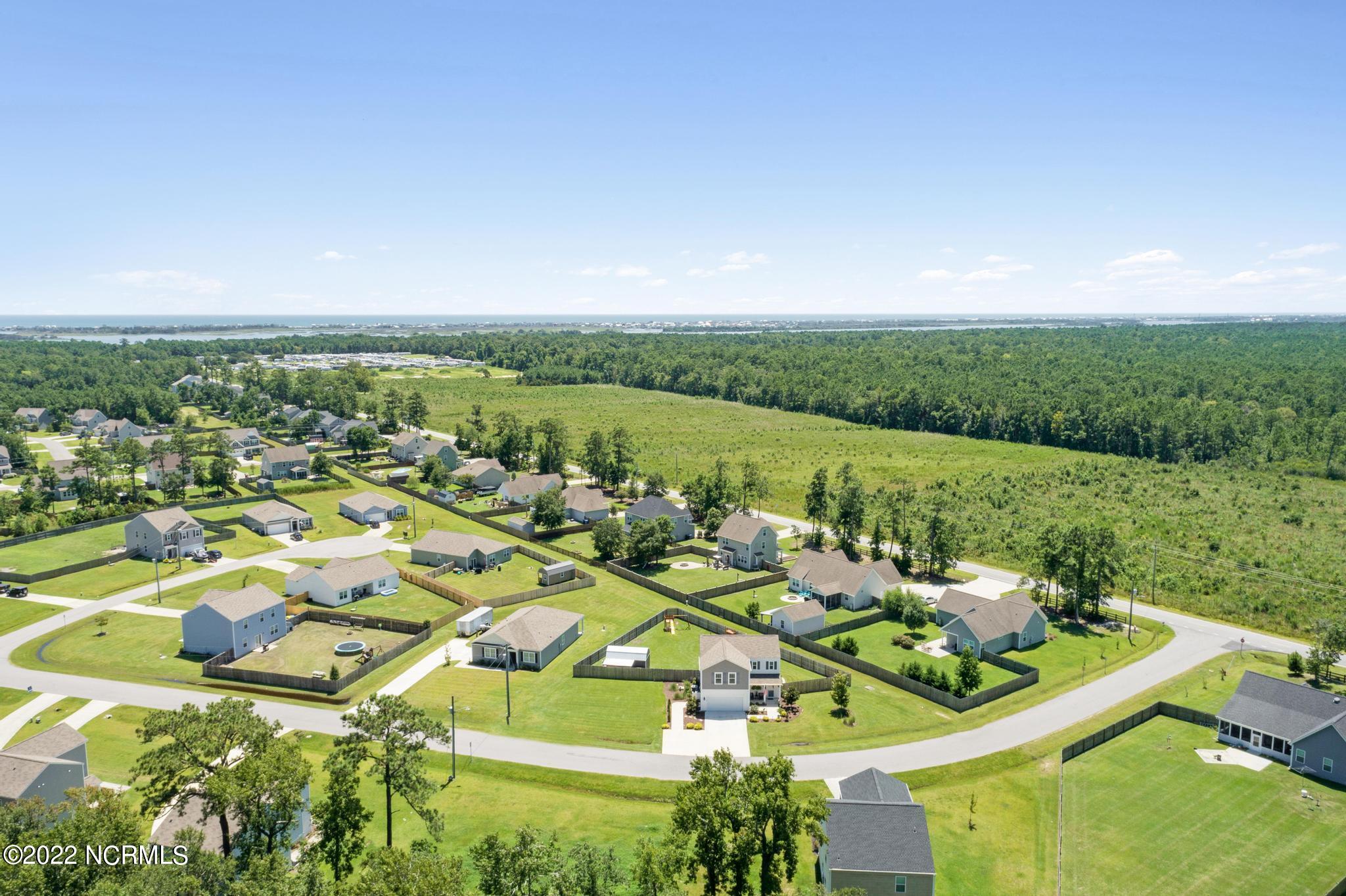 Aerial view of a coastal neighborhood with fenced yards, curving streets, and water in the distance.
