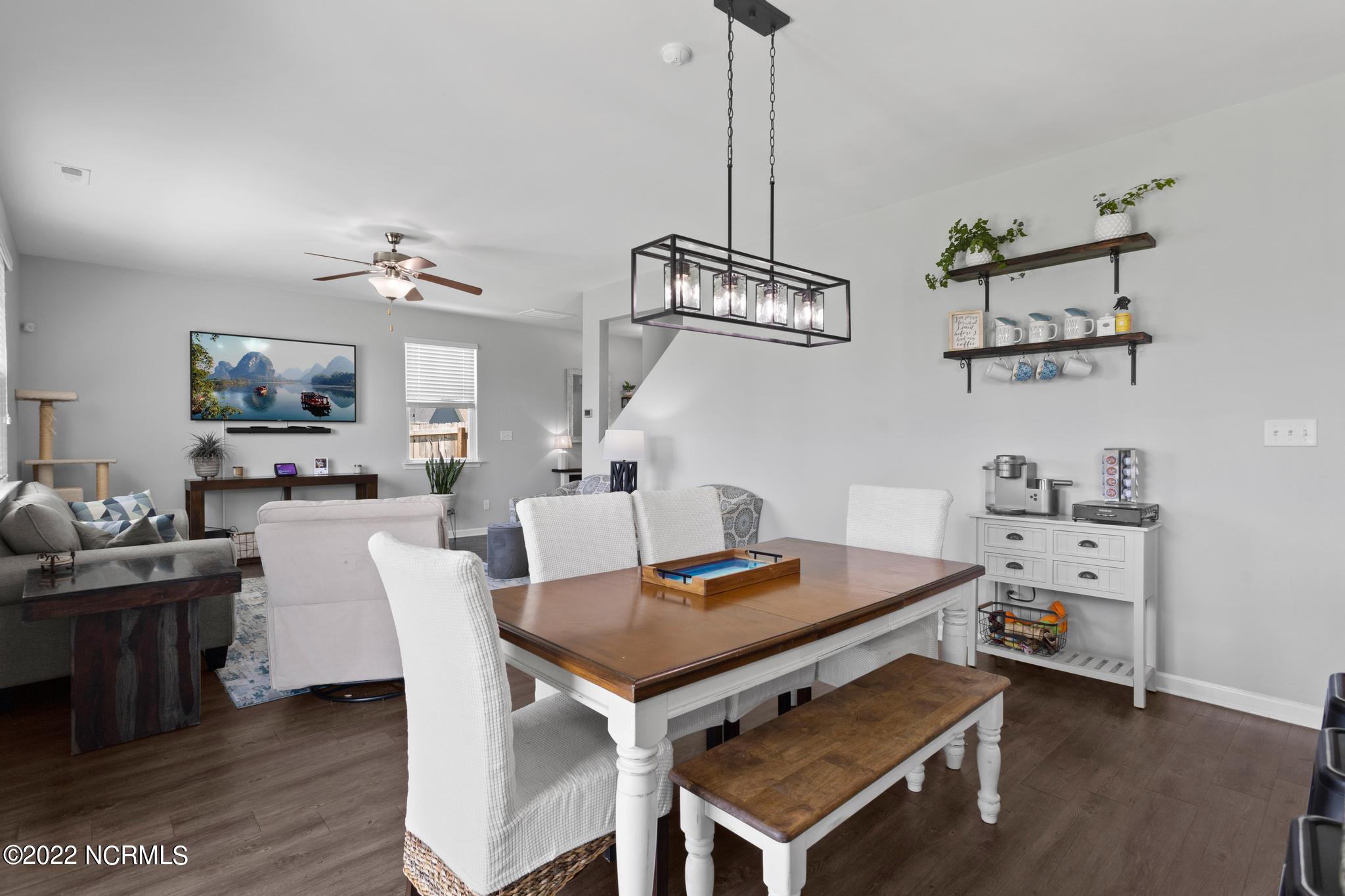 Open-plan dining and living room with a wooden table, white chairs, bench, and dark rectangular chandelier.