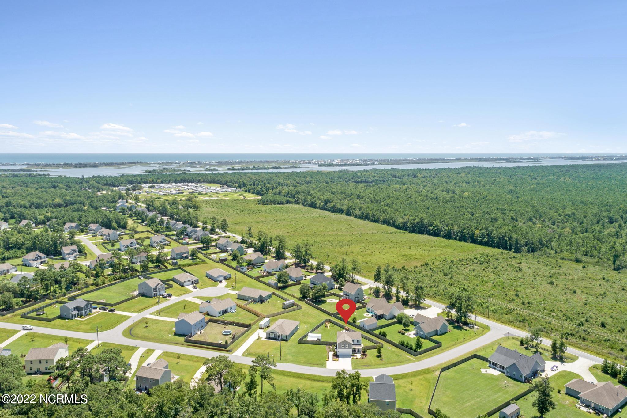 Aerial view of the neighborhood and marked home, with surrounding forest and coastal water beyond.