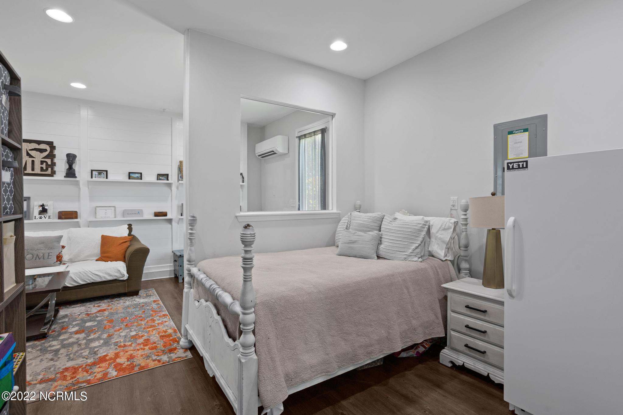 Bedroom with a white four-poster bed, adjoining sitting area, built-in shelves, and patterned rug.