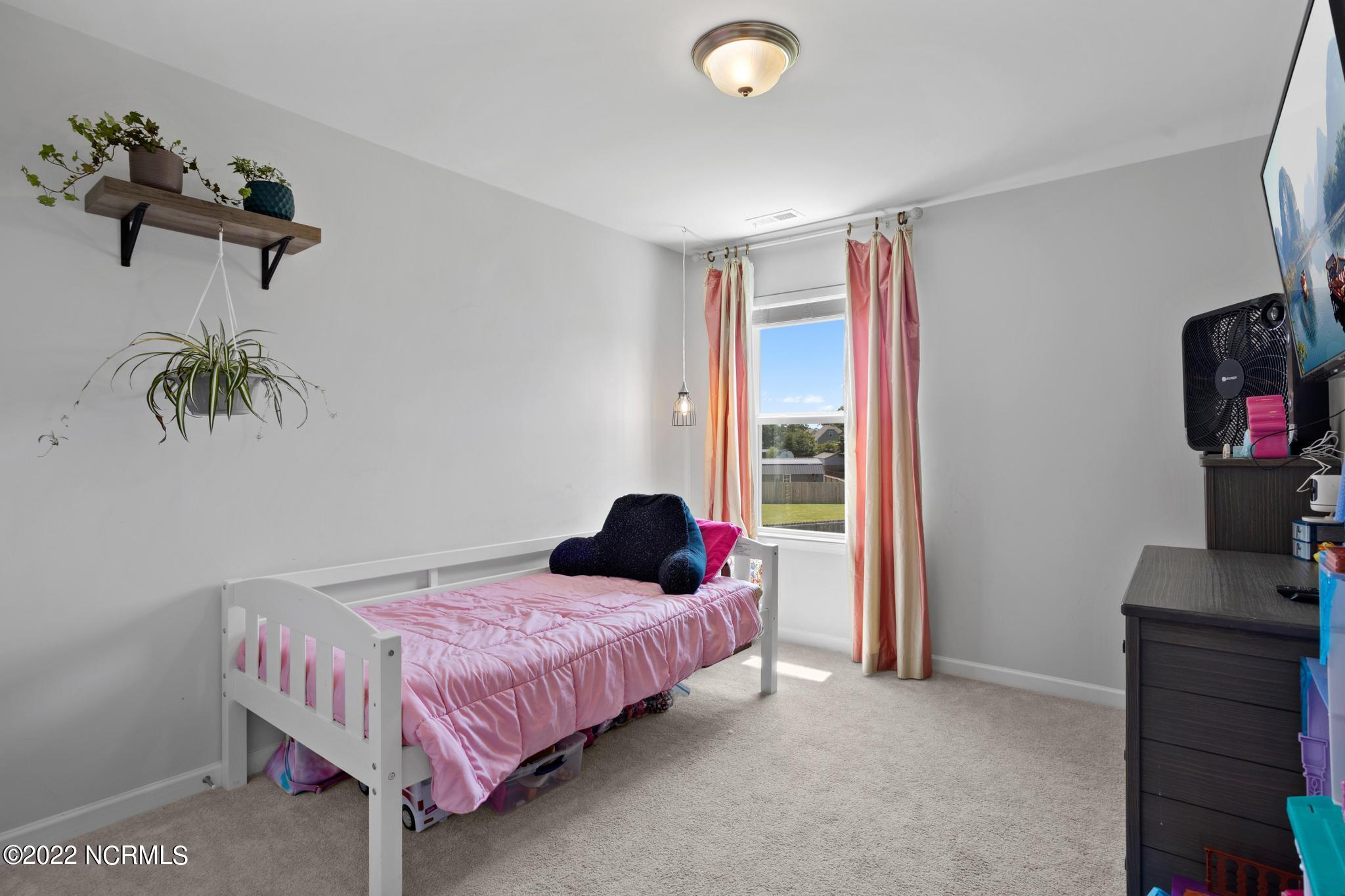 Bedroom with a white daybed, pink bedding, coral curtains, and wall-mounted plant shelves.