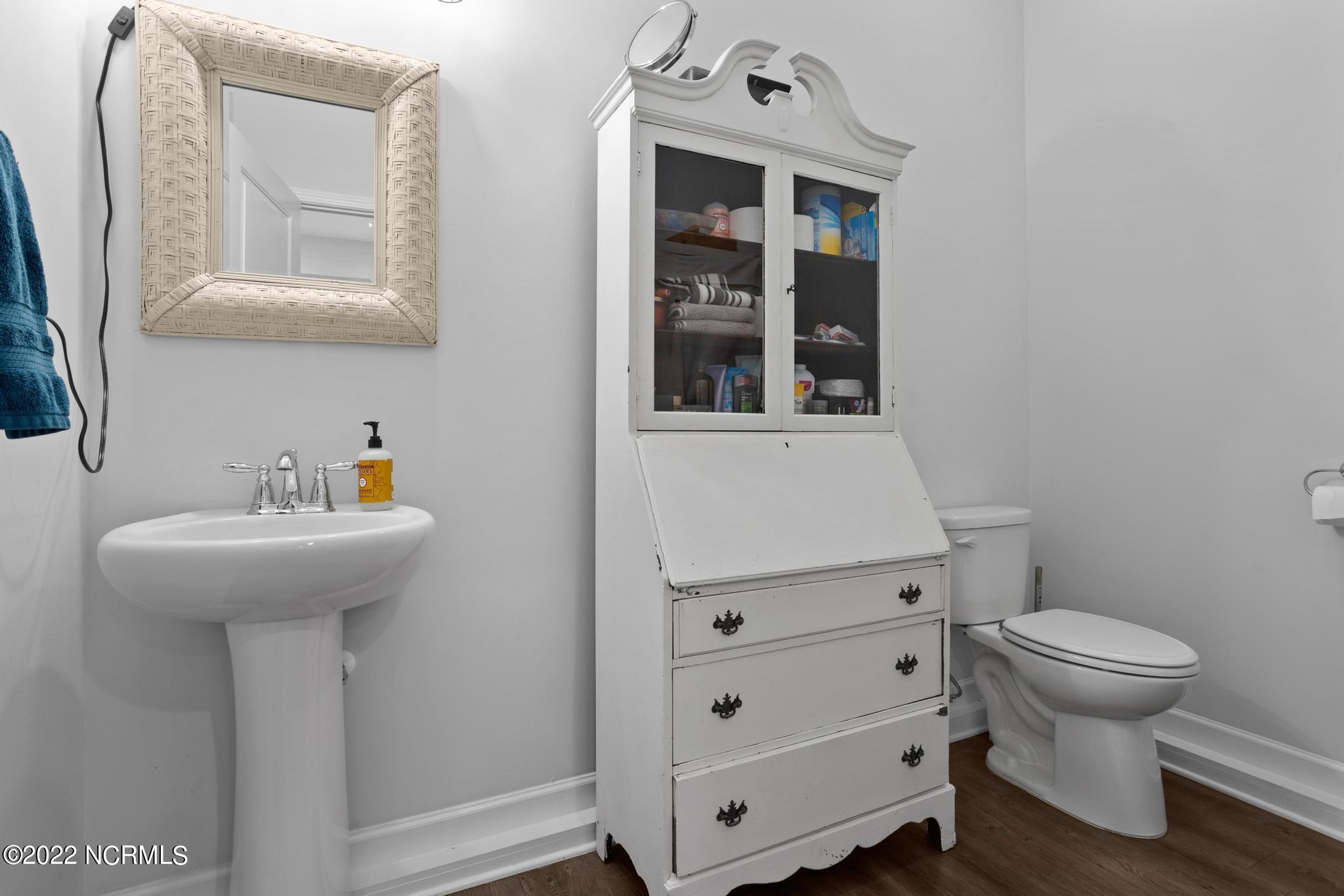 Bathroom with a pedestal sink, toilet, and tall white cabinet with glass doors.