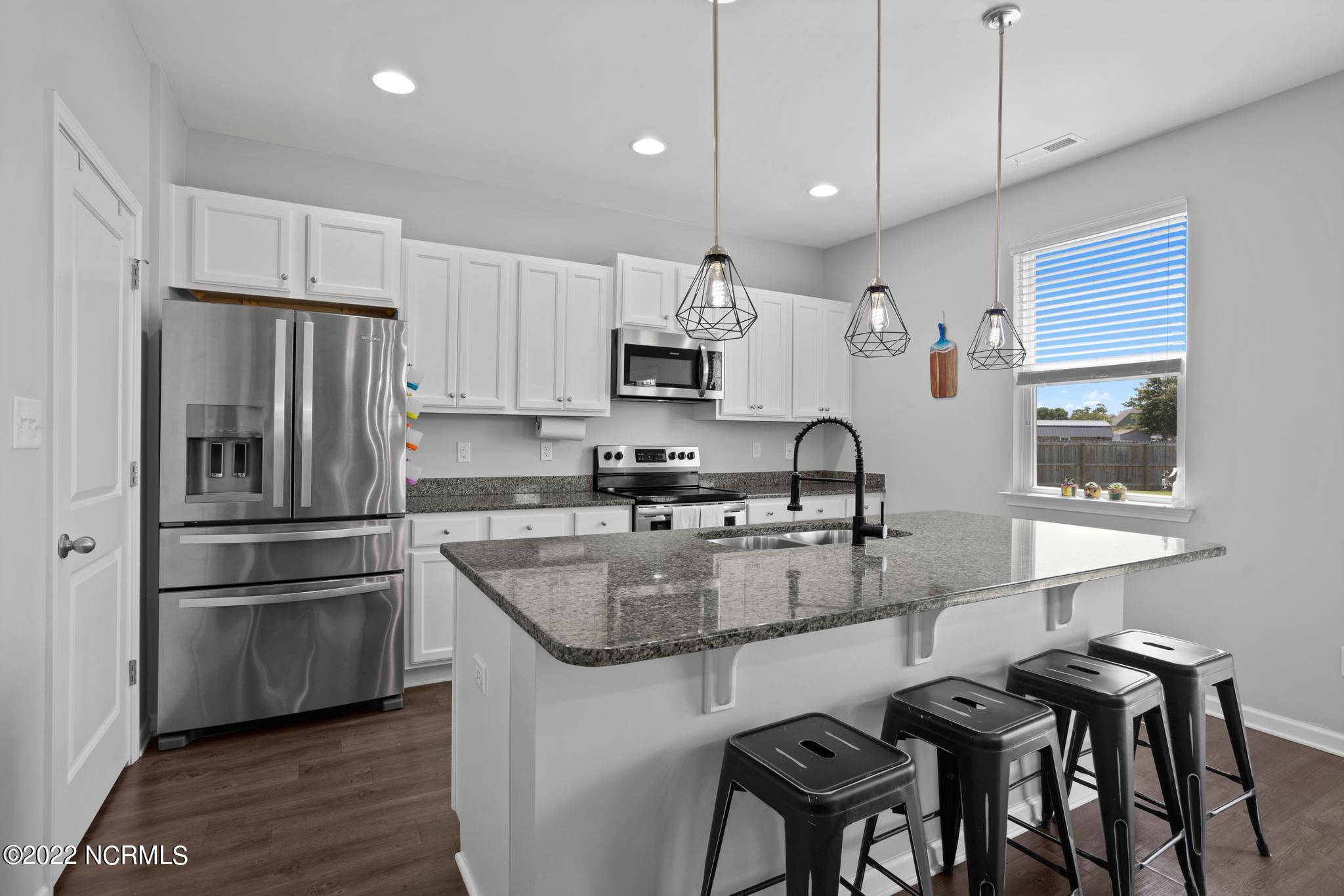 Kitchen with a granite island, black bar stools, white cabinets, and stainless steel appliances.
