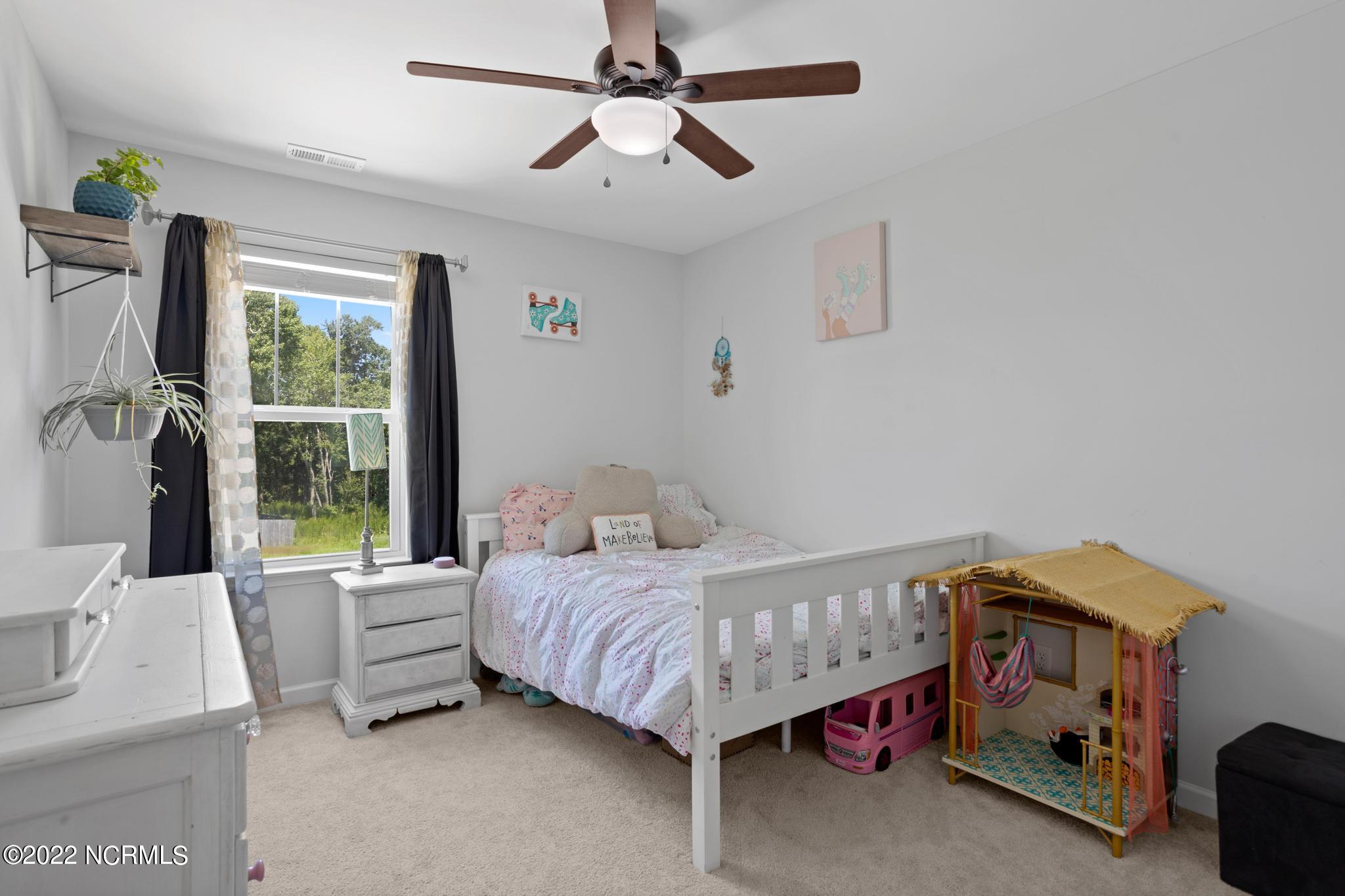 Child’s bedroom with a white daybed, large curtained window, and playhouse beside the bed.