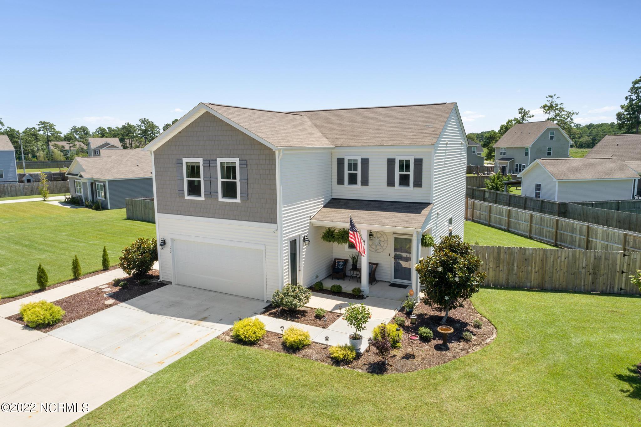 Two-story white and gray house with an attached garage, landscaped front yard, and American flag.