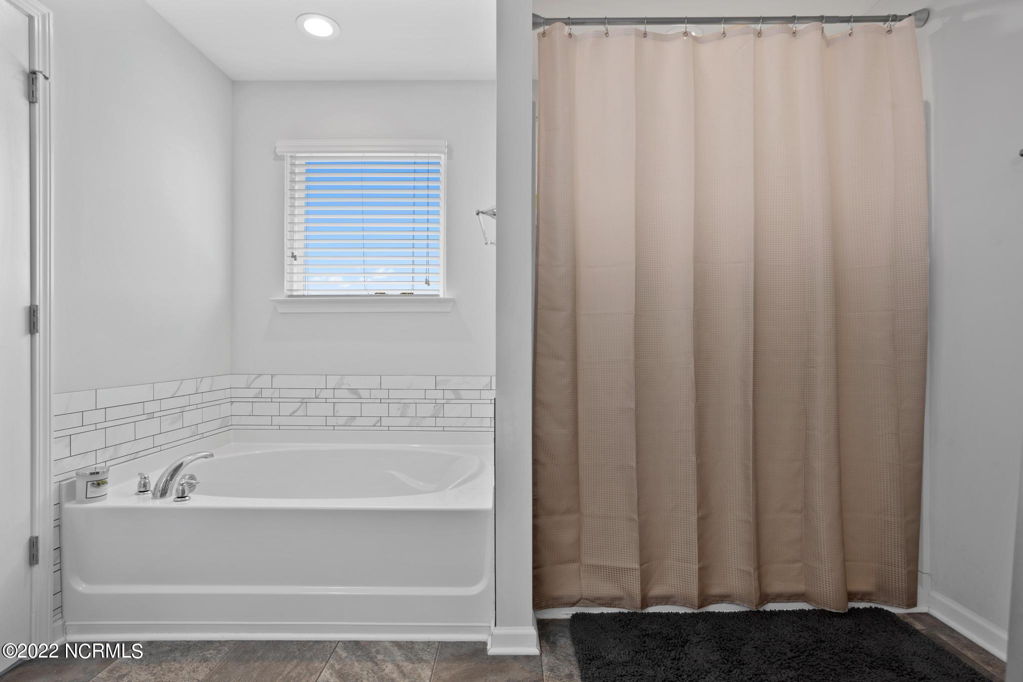 Bathroom with a white bathtub, veined subway tile, window blinds, and beige shower curtain.