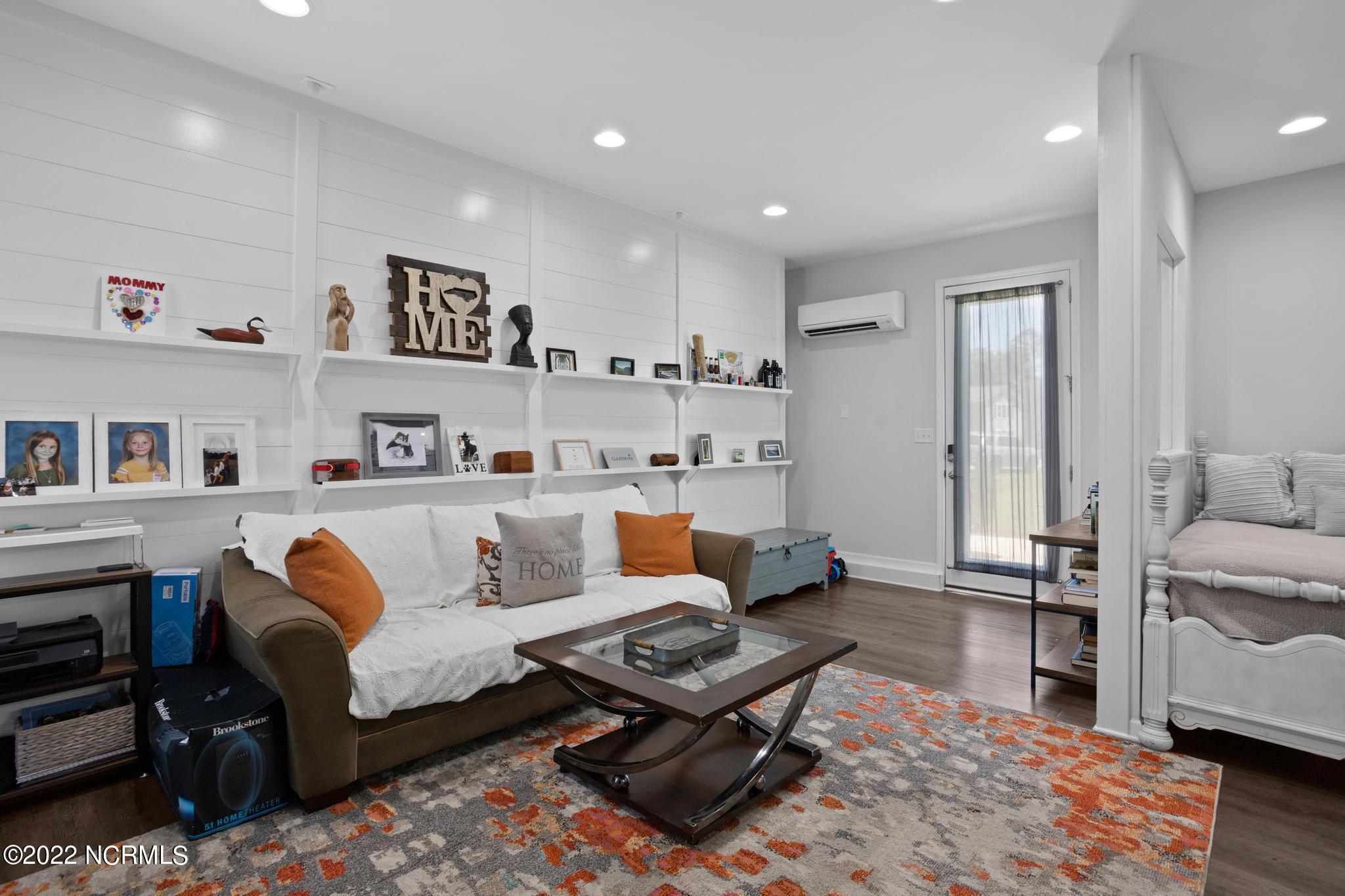 Living room with white shiplap shelves, a sofa with rust cushions, and a glass-top coffee table beside a bed.