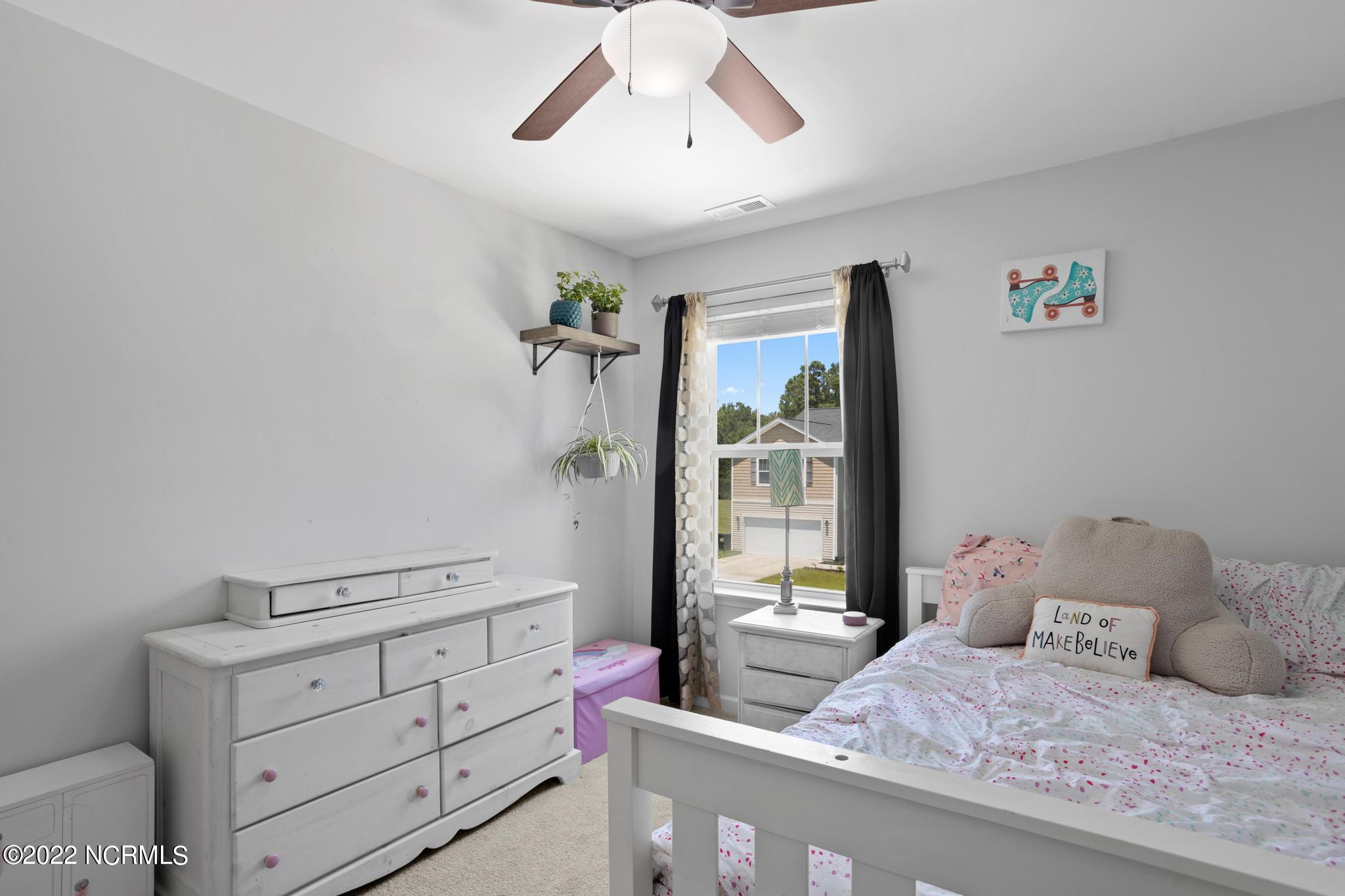 Bedroom with pink-patterned bedding, a white dresser, and a window framed by dark curtains.